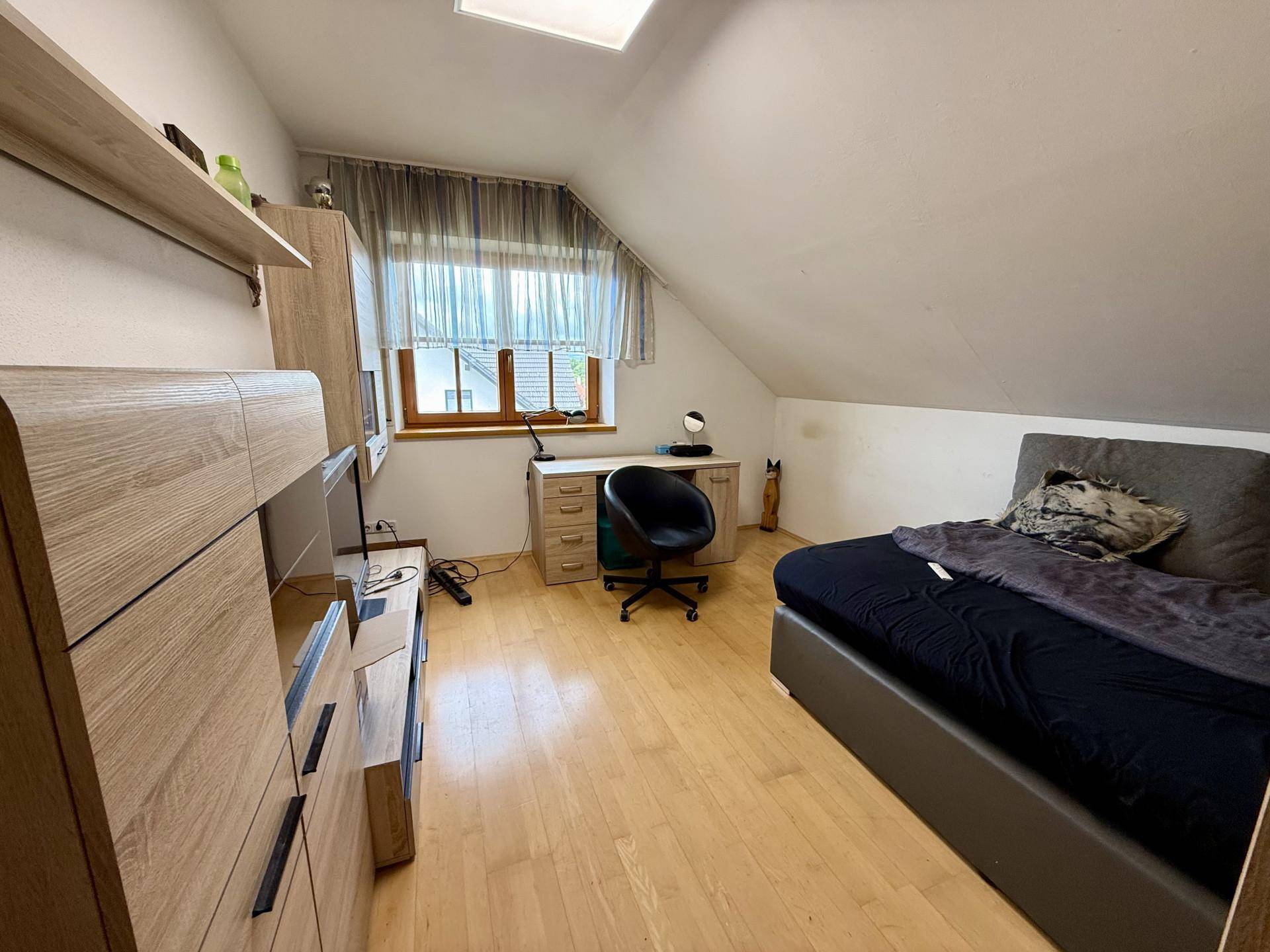 Dachgeschosszimmer mit Holzboden, Schreibtisch und Bett unter einer charakteristischen Dachschräge.