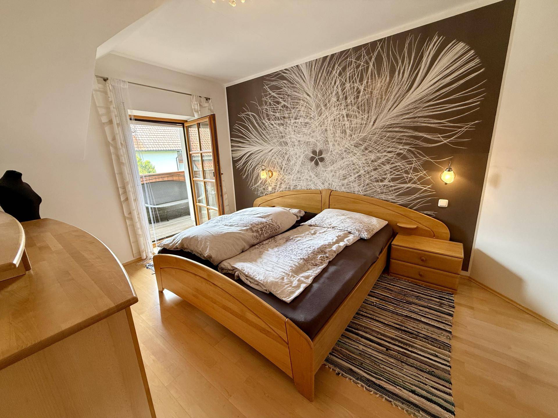 Helles Schlafzimmer mit Holzboden, Doppelbett und direktem Zugang zu einem Balkon.