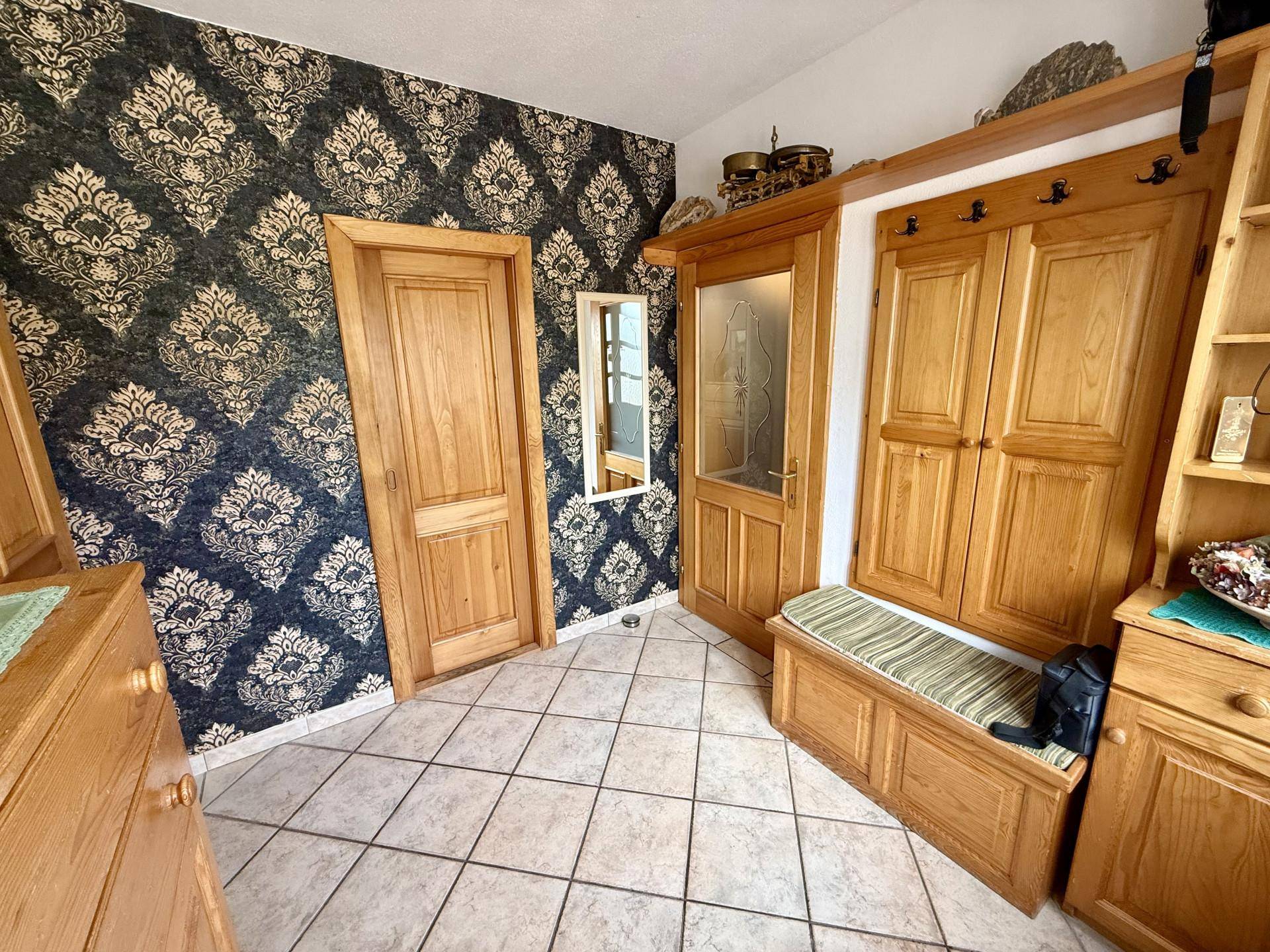 Eingangsbereich mit Fliesenboden, Holzgarderobe und auffälliger gemusterter Tapete.