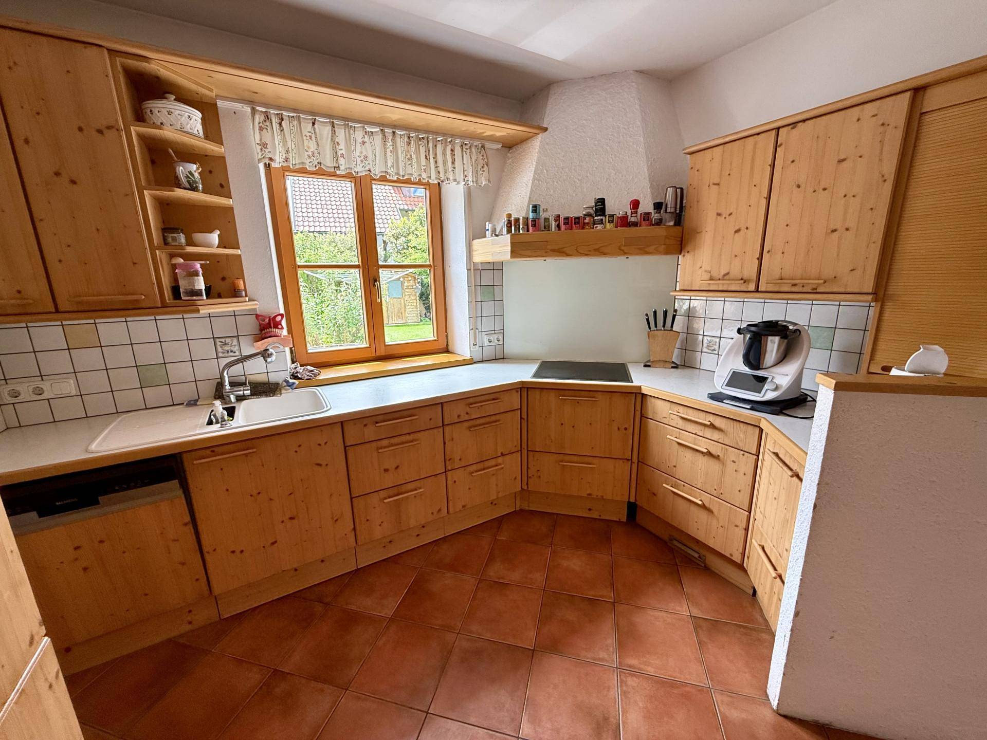 Rustikale Küche mit Holzschränken, Fliesenboden und Fenster mit Blick in den Garten.
