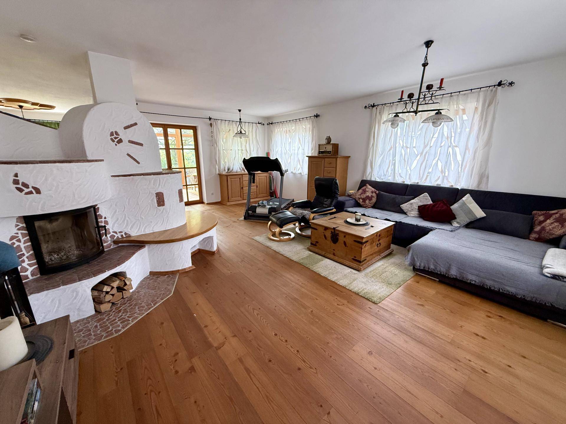 Gemütliches Wohnzimmer mit Holzboden, großem Sofa und traditionellem Kaminofen als Blickfang.