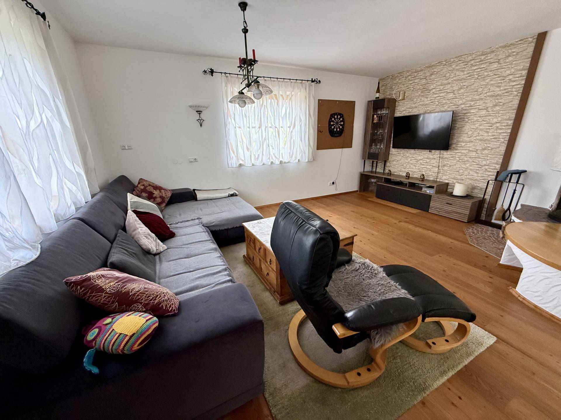 Gemütliches Wohnzimmer mit großem Sofa, Holzboden und Fernseher an einer strukturierten Wand.