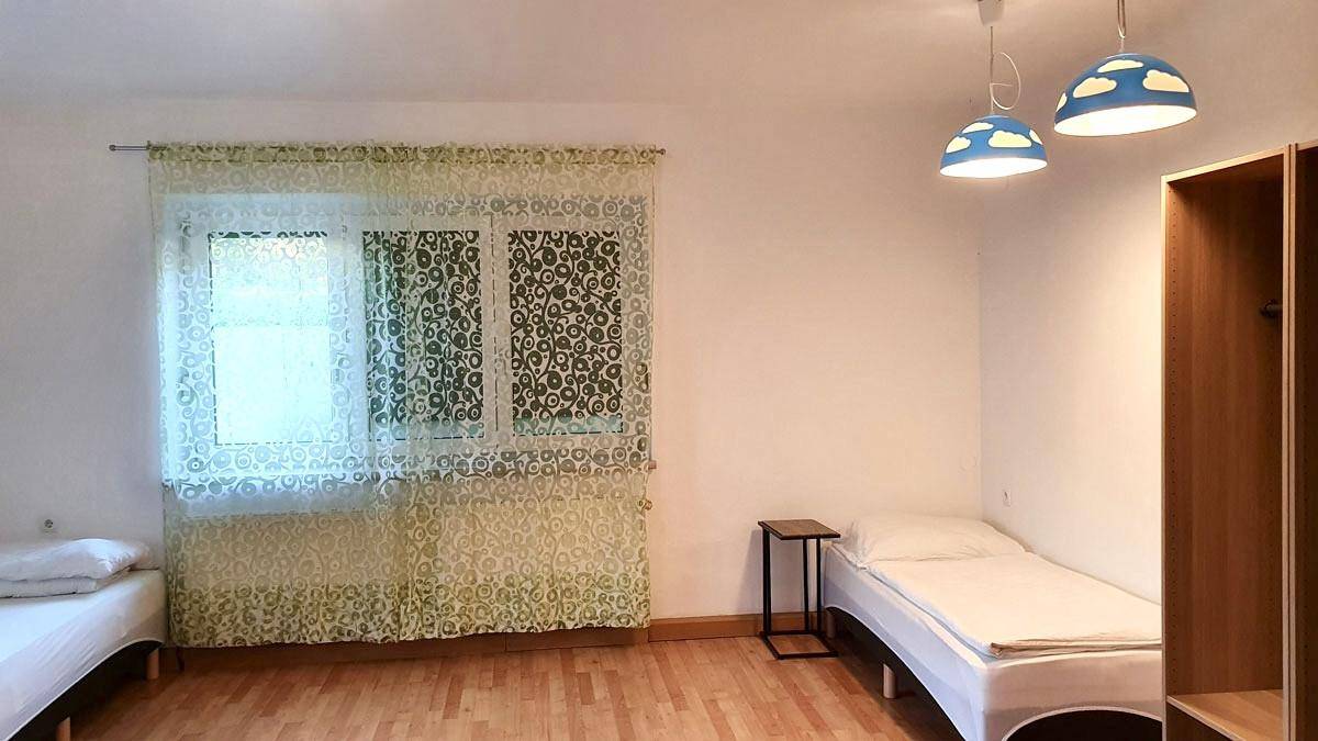 Helles Schlafzimmer mit zwei Einzelbetten, Holzfußboden und dekorativen Vorhängen am Fenster.