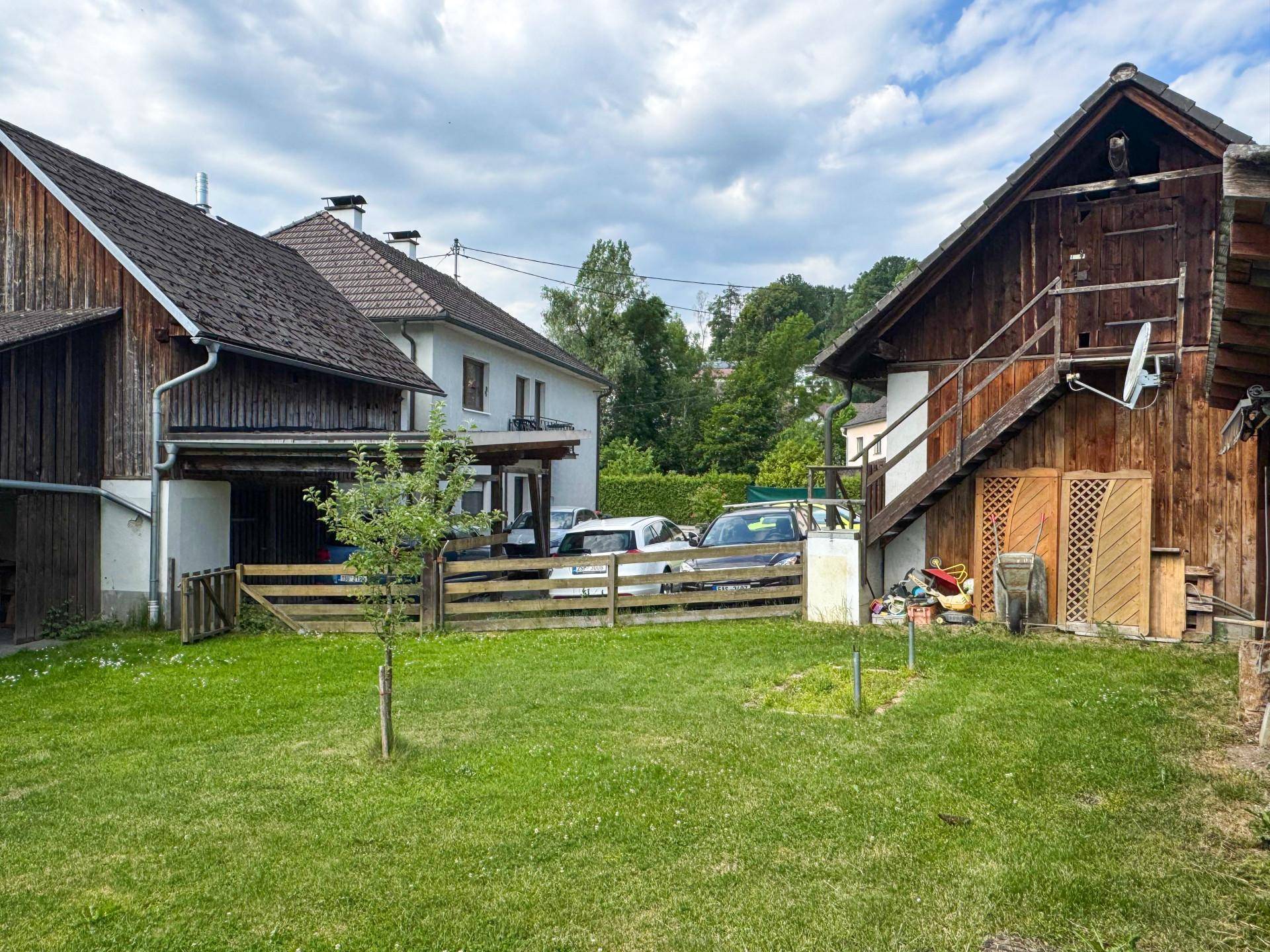 Hinterhofbereich mit Rasenfläche, Holzscheune und Blick auf die umliegende Natur.
