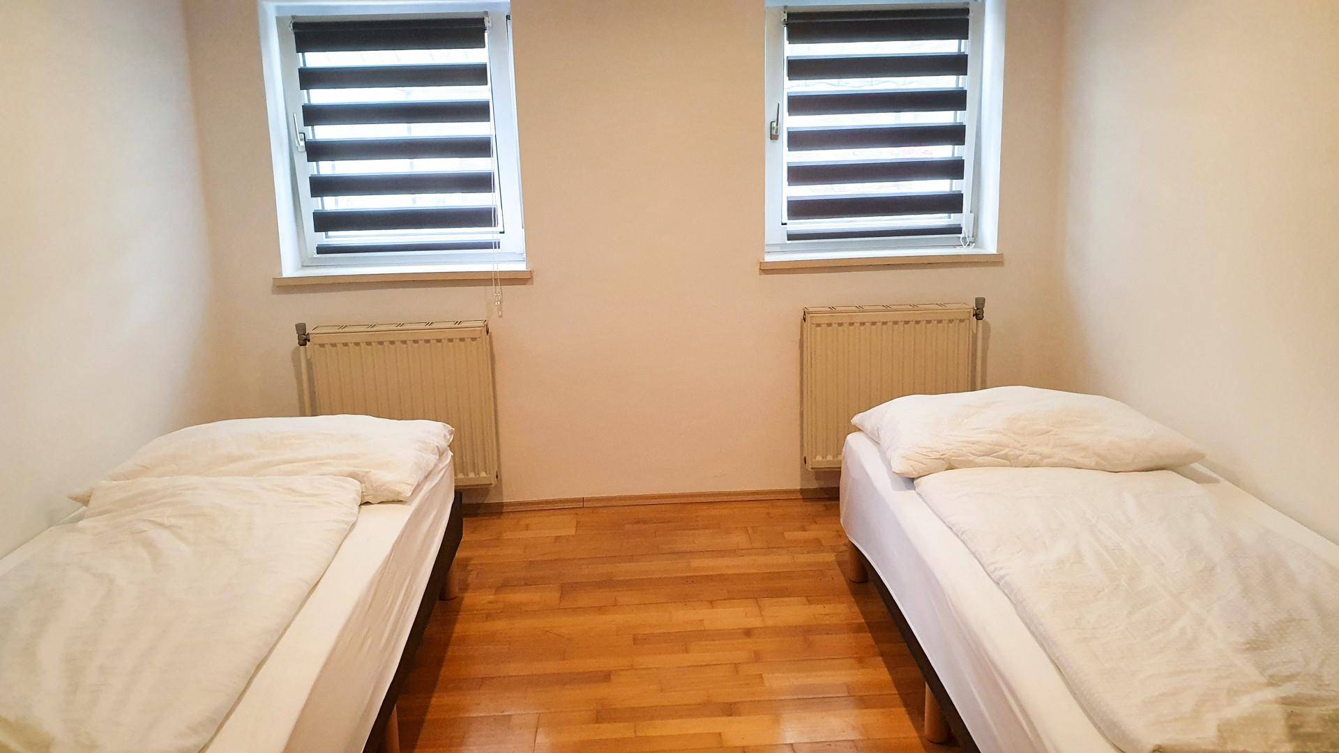 Helles Schlafzimmer mit zwei Einzelbetten, Holzfußboden und Jalousien an den Fenstern.