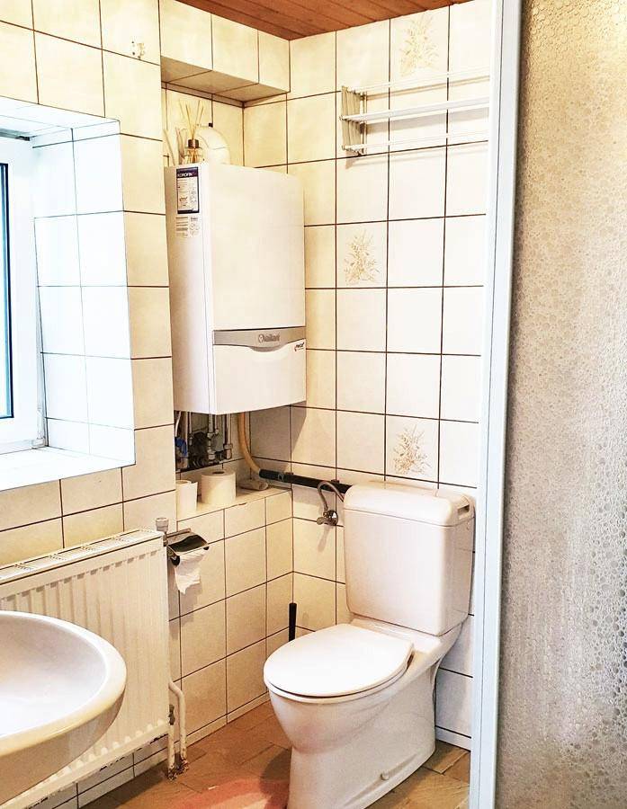 Kleines WC mit Fliesen, Toilette, Waschbecken und einem Wandheizkessel.