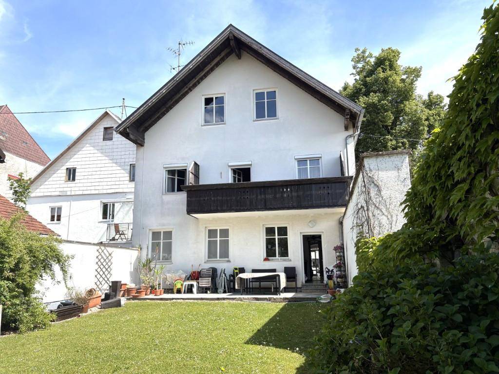 Rückseite eines weißen Hauses mit Balkon und Terrasse, die auf einen gepflegten Rasen blicken.