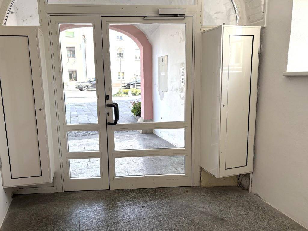 Heller Eingangsbereich mit Glastüren, die zur Straße führen, und zwei weißen Schränken.