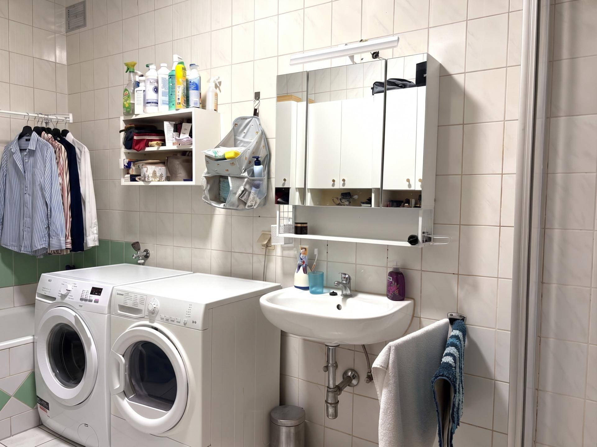 Badezimmer mit Waschbecken, Spiegelschrank, Waschmaschine, Trockner und Duschbereich.