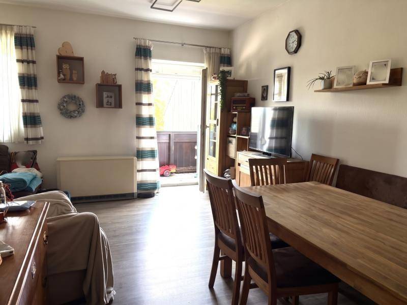 Kombinierter Wohn- und Essbereich mit Holztisch, Sofa und Zugang zu einem Balkon.