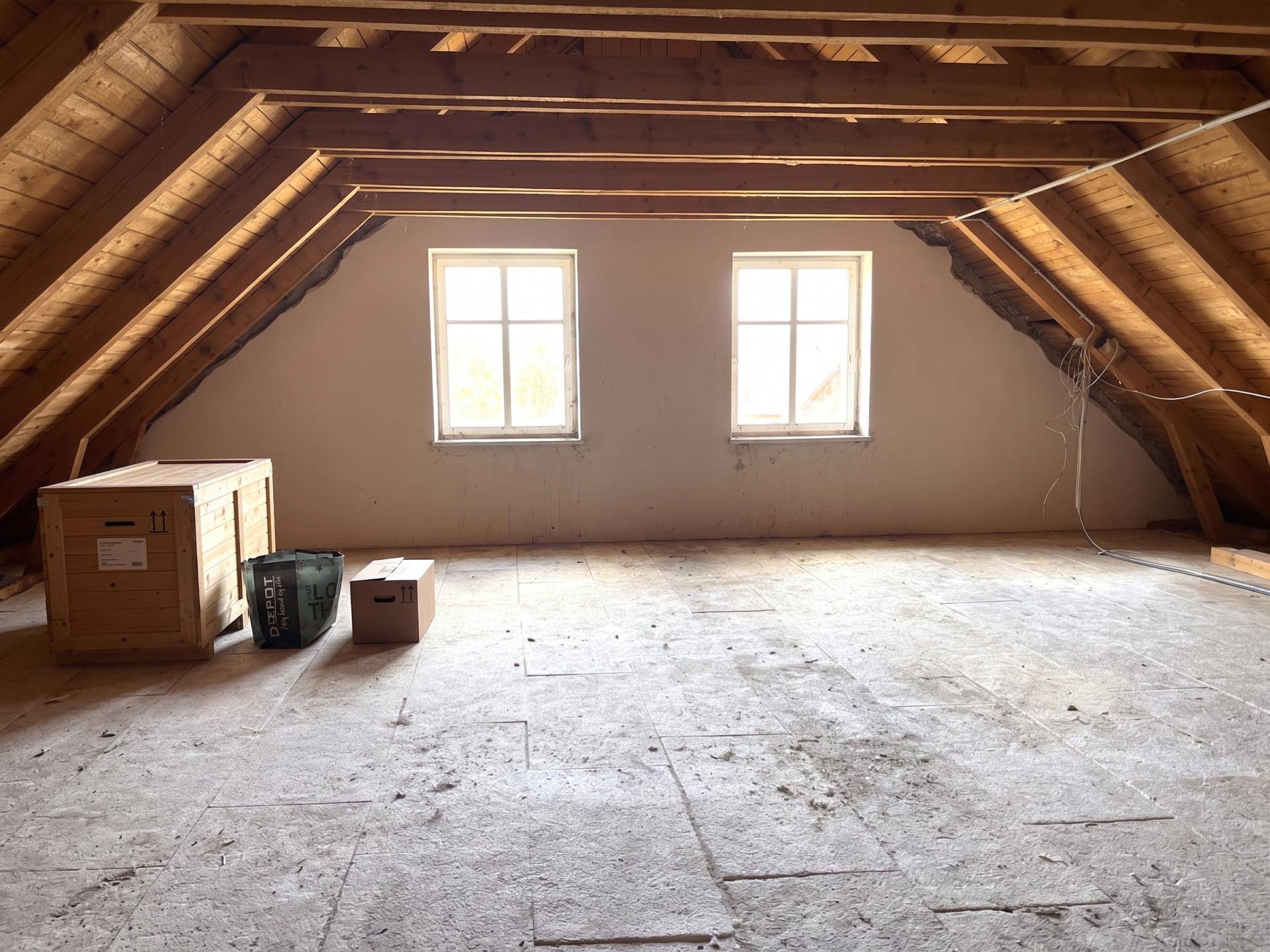 Unausgebauter Dachboden mit sichtbaren Holzbalken und zwei Fenstern, bereit zum Ausbau.