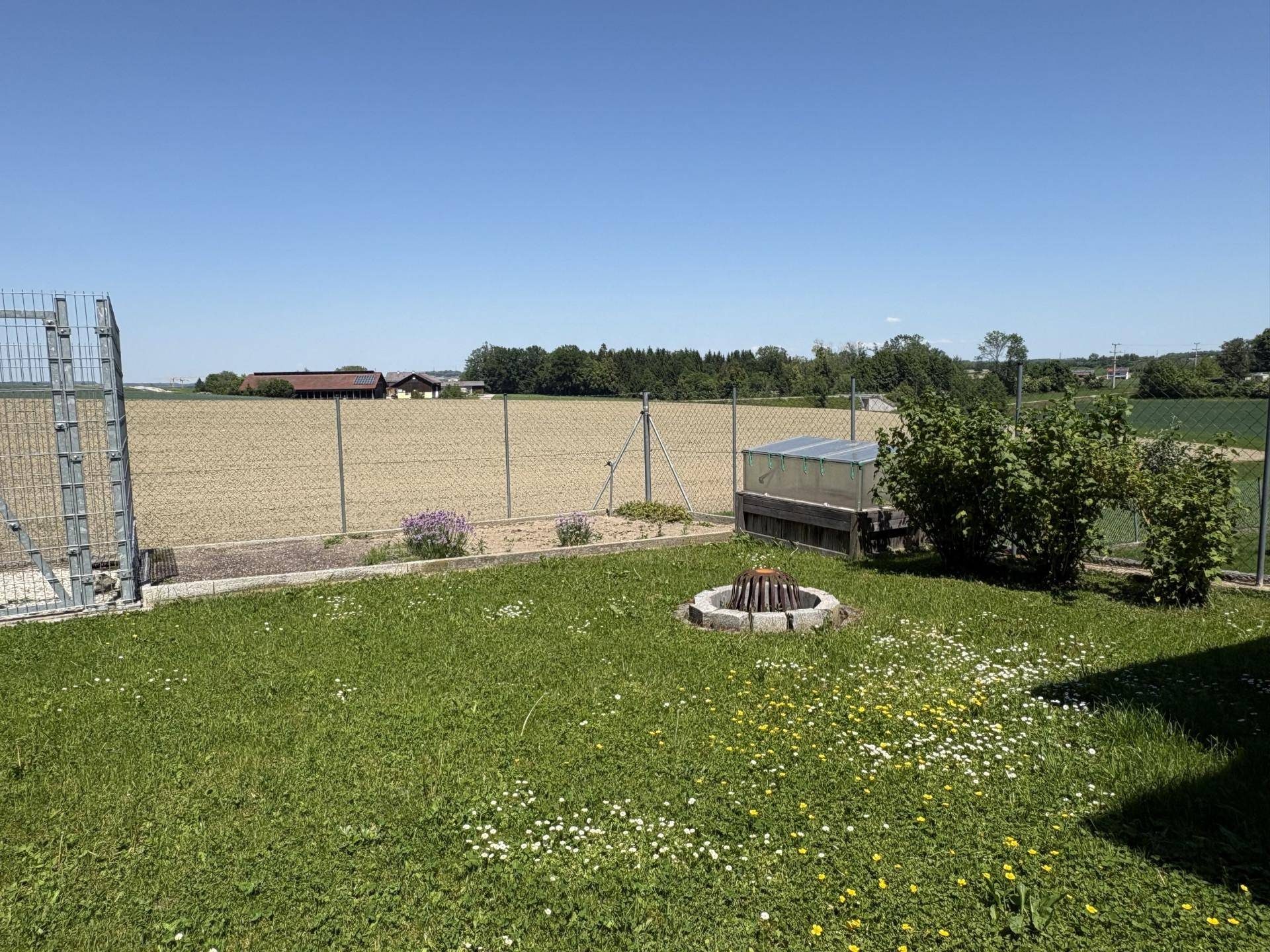 Grüner Garten mit Rasenfläche, Feuerstelle und weitem Blick über die umliegenden Felder.