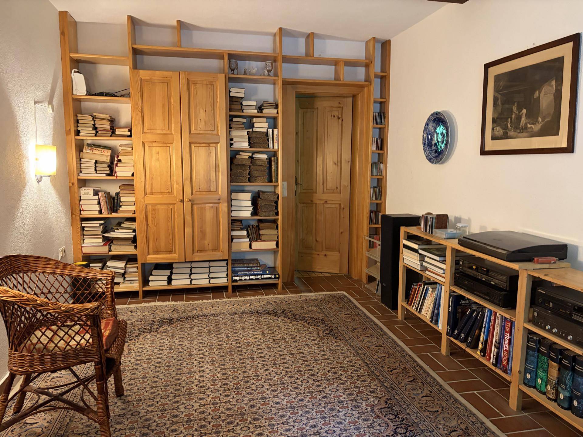 Bibliothek oder Arbeitszimmer mit eingebauten Holzregalen voller Bücher und einem gemütlichen Teppich.