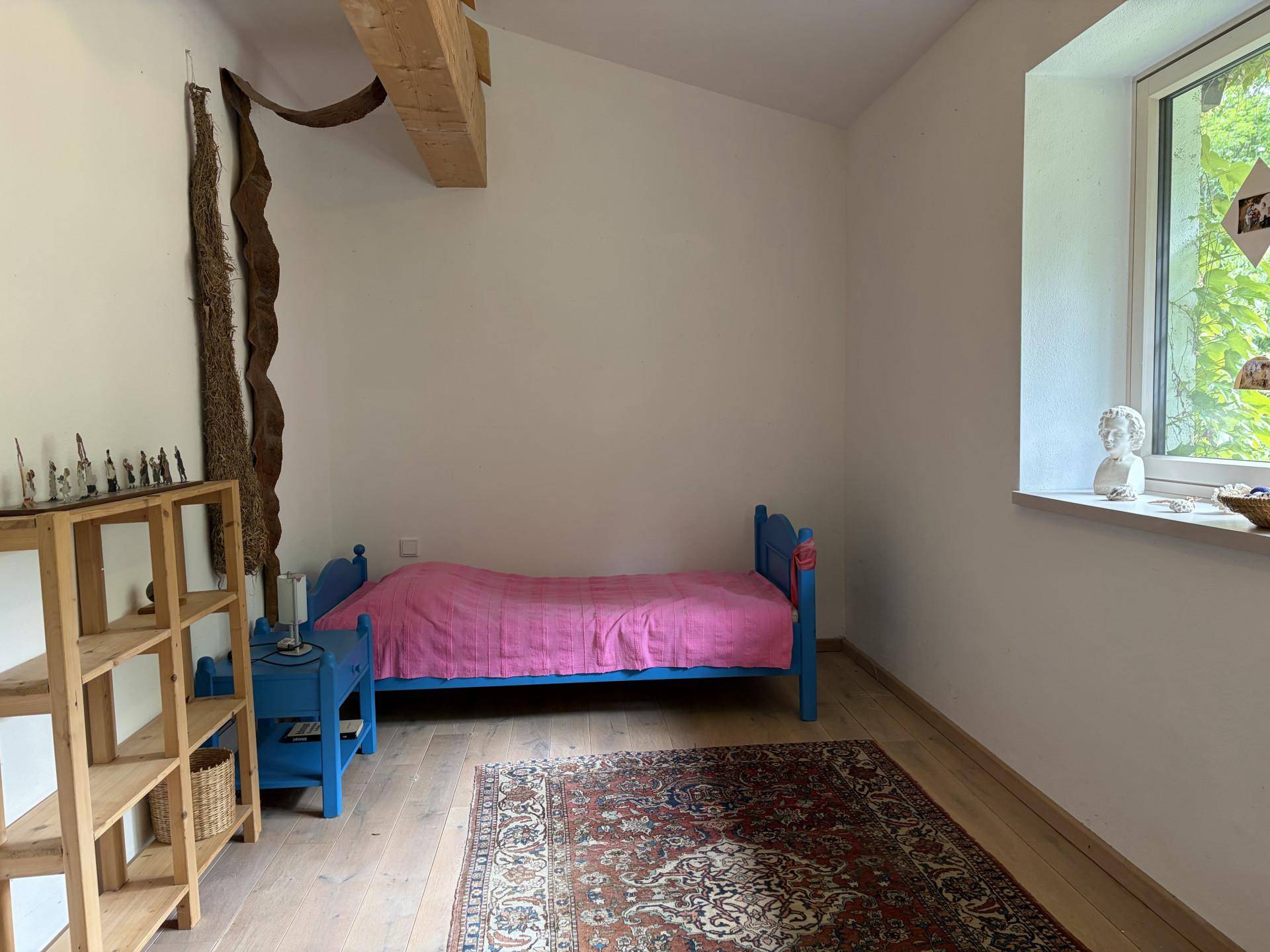 Gemütliches Schlafzimmer im Dachgeschoss mit Holzbalken, Einzelbett und Fenster mit Blick ins Grüne.