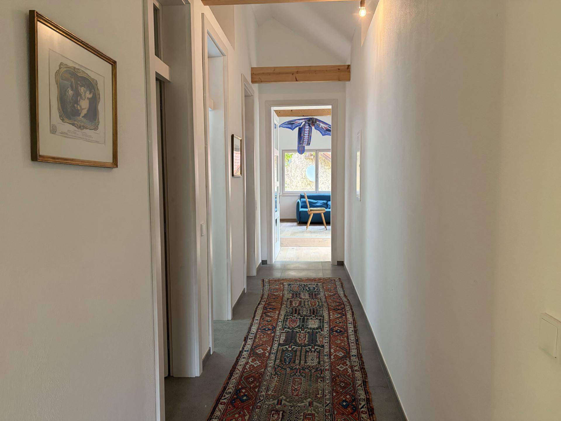 Langer, heller Flur im Dachgeschoss mit Teppichläufer und Holzbalken, der verschiedene Zimmer verbindet.