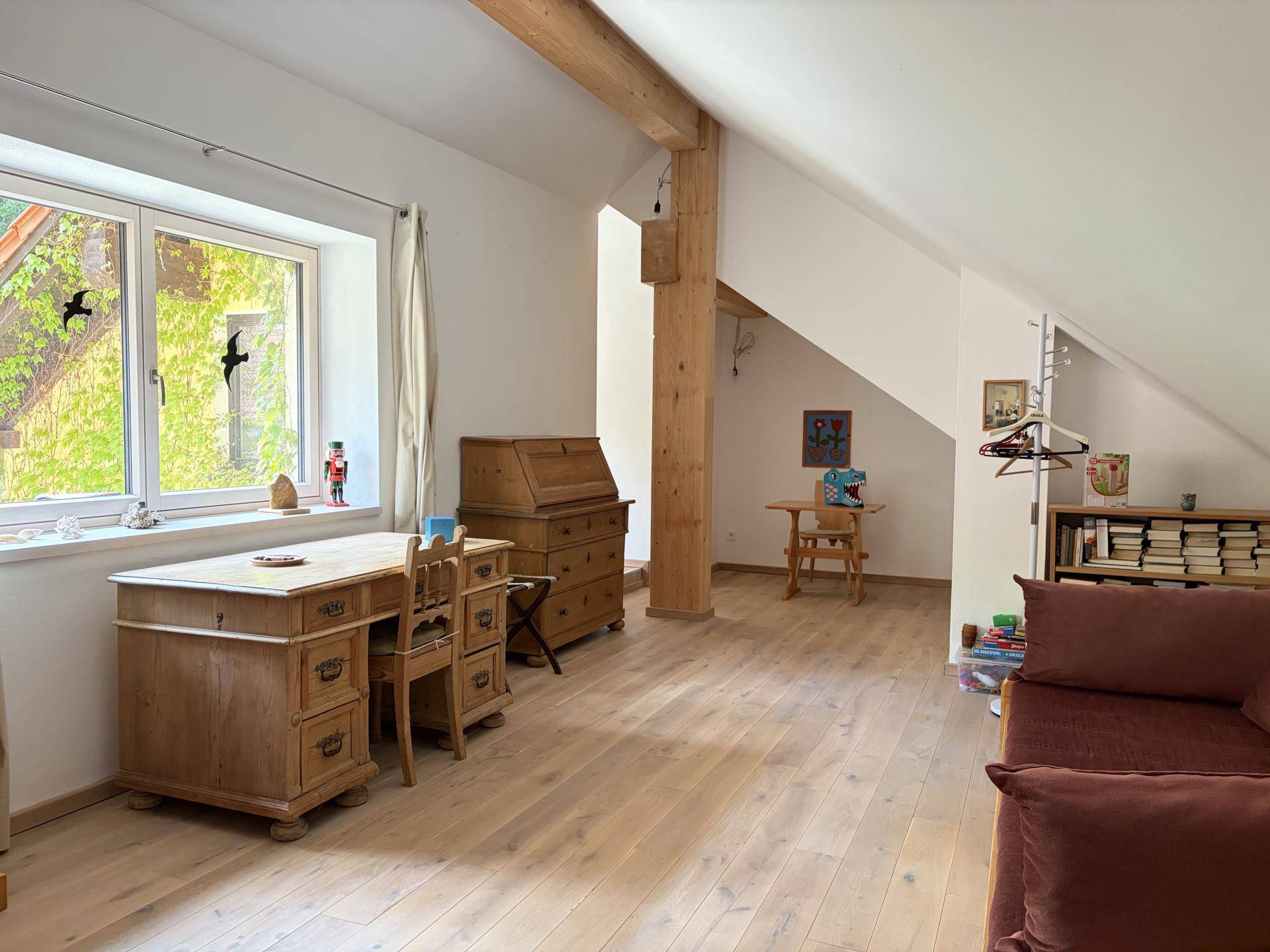 Geräumiges Arbeitszimmer im Dachgeschoss mit Holzbalken, großem Schreibtisch und viel natürlichem Licht.