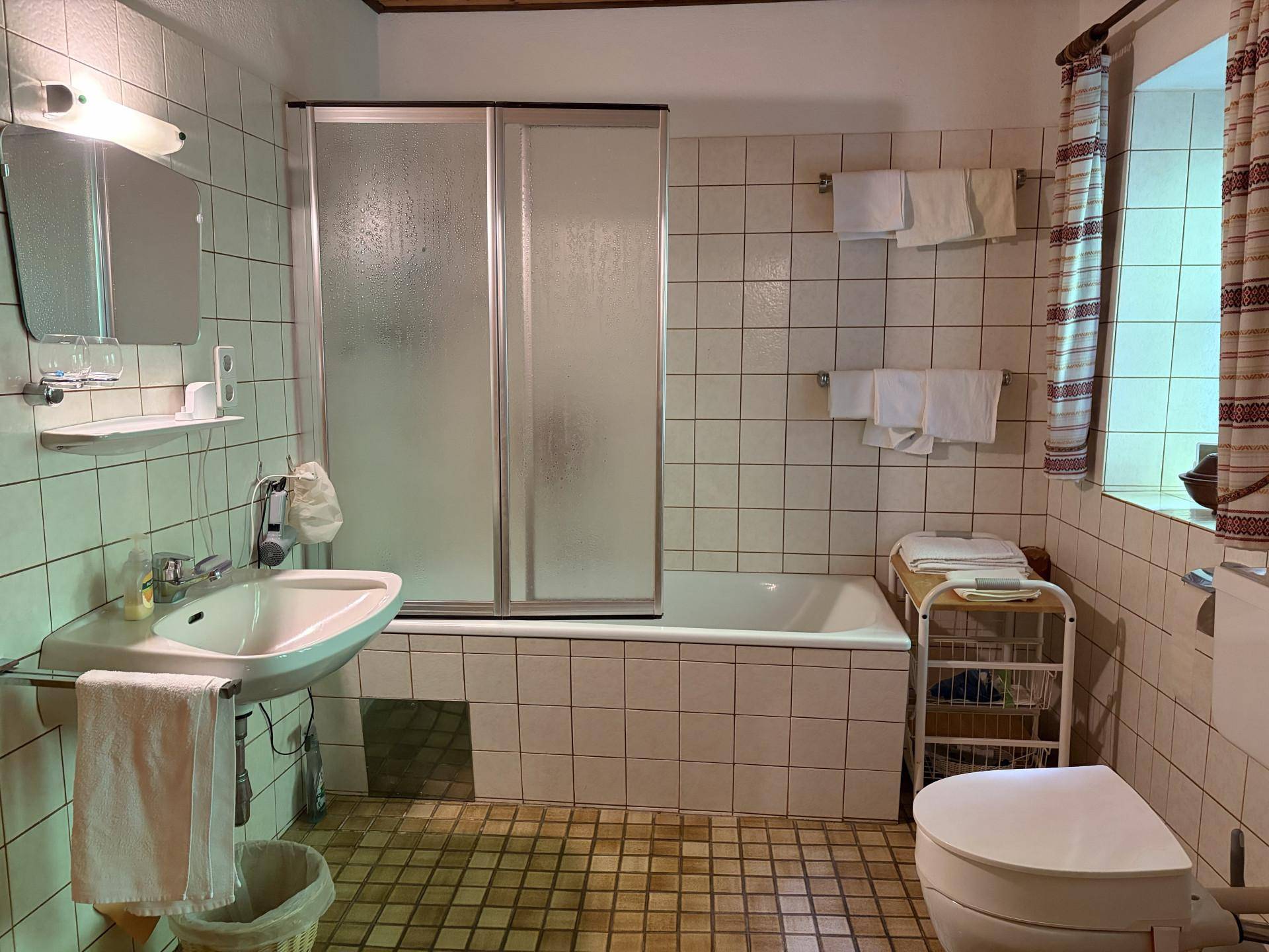 Traditionelles Badezimmer mit Badewanne, Duschkabine und Waschbecken, komplett gefliest in hellem Ton.