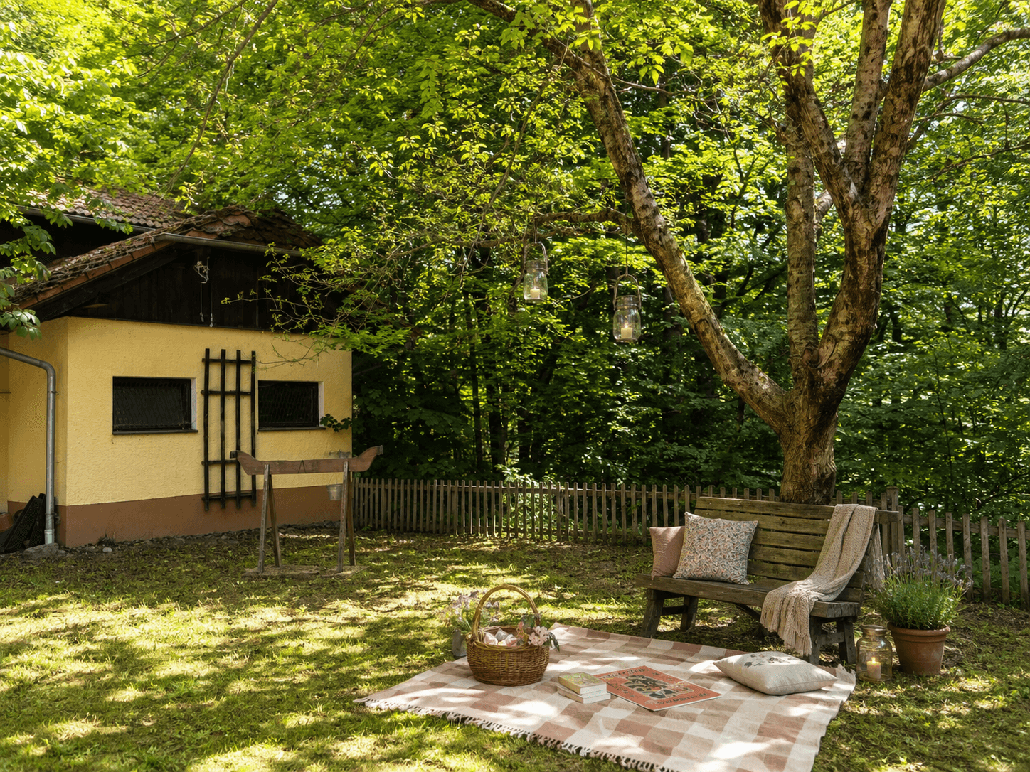Gemütlicher Gartenbereich mit Sitzbank unter einem Baum und Picknickdecke, umgeben von viel Grün.