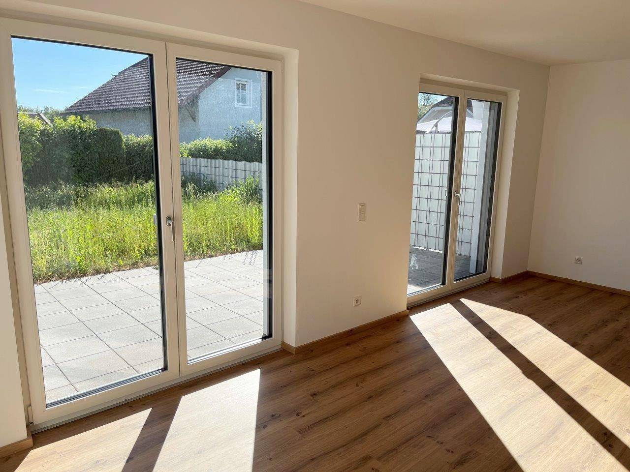 Heller Wohnraum mit großen Terrassentüren, Laminatboden und Blick ins Grüne.