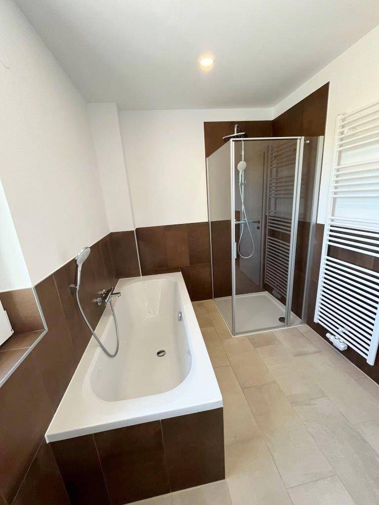 Modernes Badezimmer mit Badewanne, Duschkabine und beheiztem Handtuchhalter.