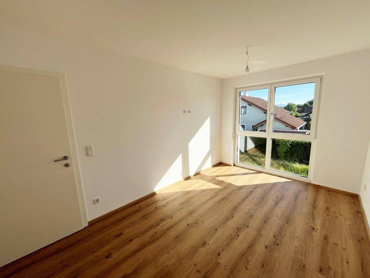 Lichtdurchflutetes Zimmer mit großem Fenster, Laminatboden und Blick auf die Nachbarschaft.