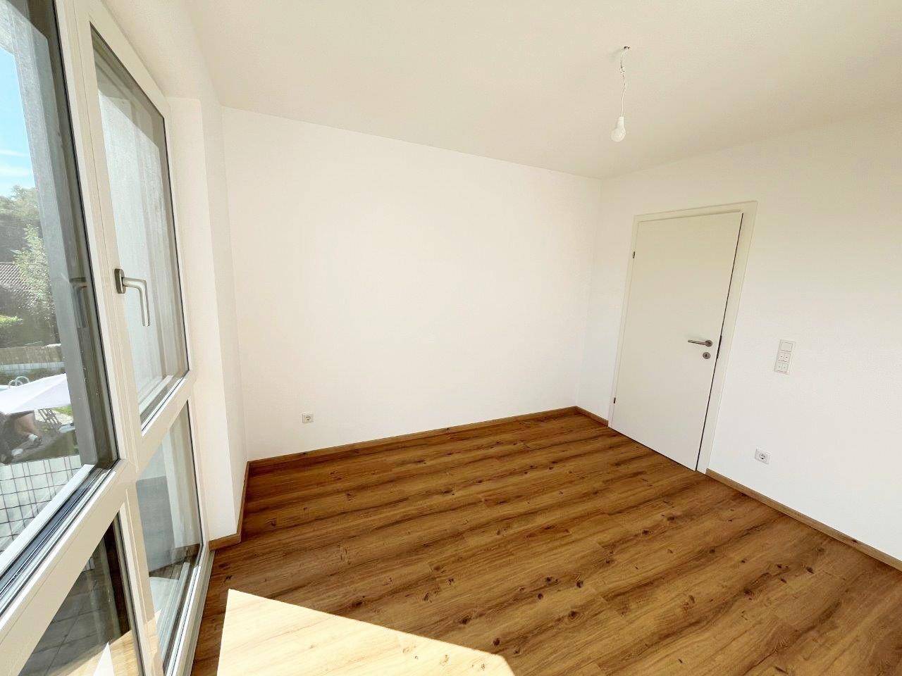 Geräumiges Zimmer mit Laminatboden, weiß gestrichenen Wänden und viel Tageslicht.