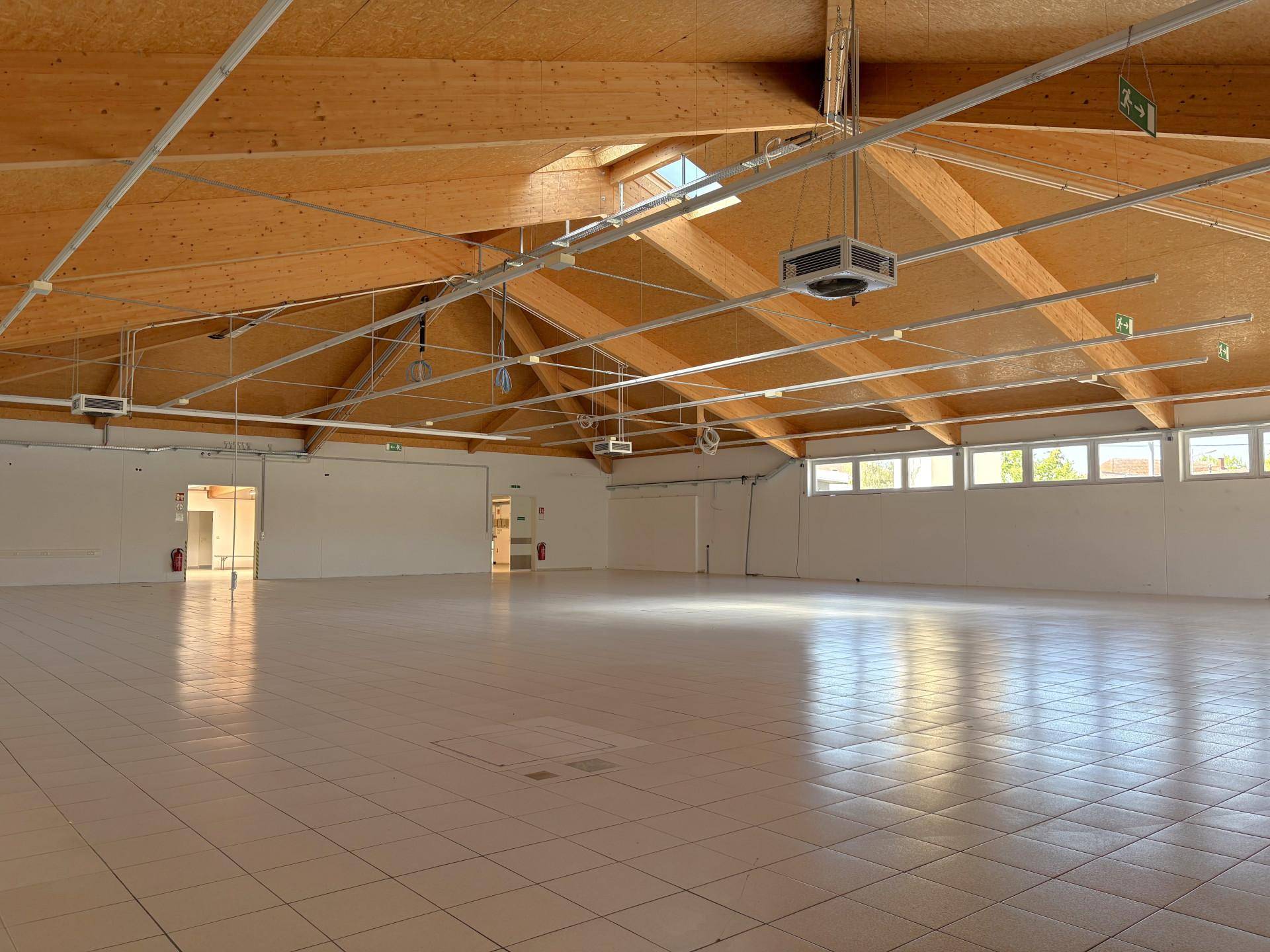Geräumiger Innenbereich mit sichtbaren Holzträgern, Fliesenboden und Oberlichtern, bietet viel Tageslicht.