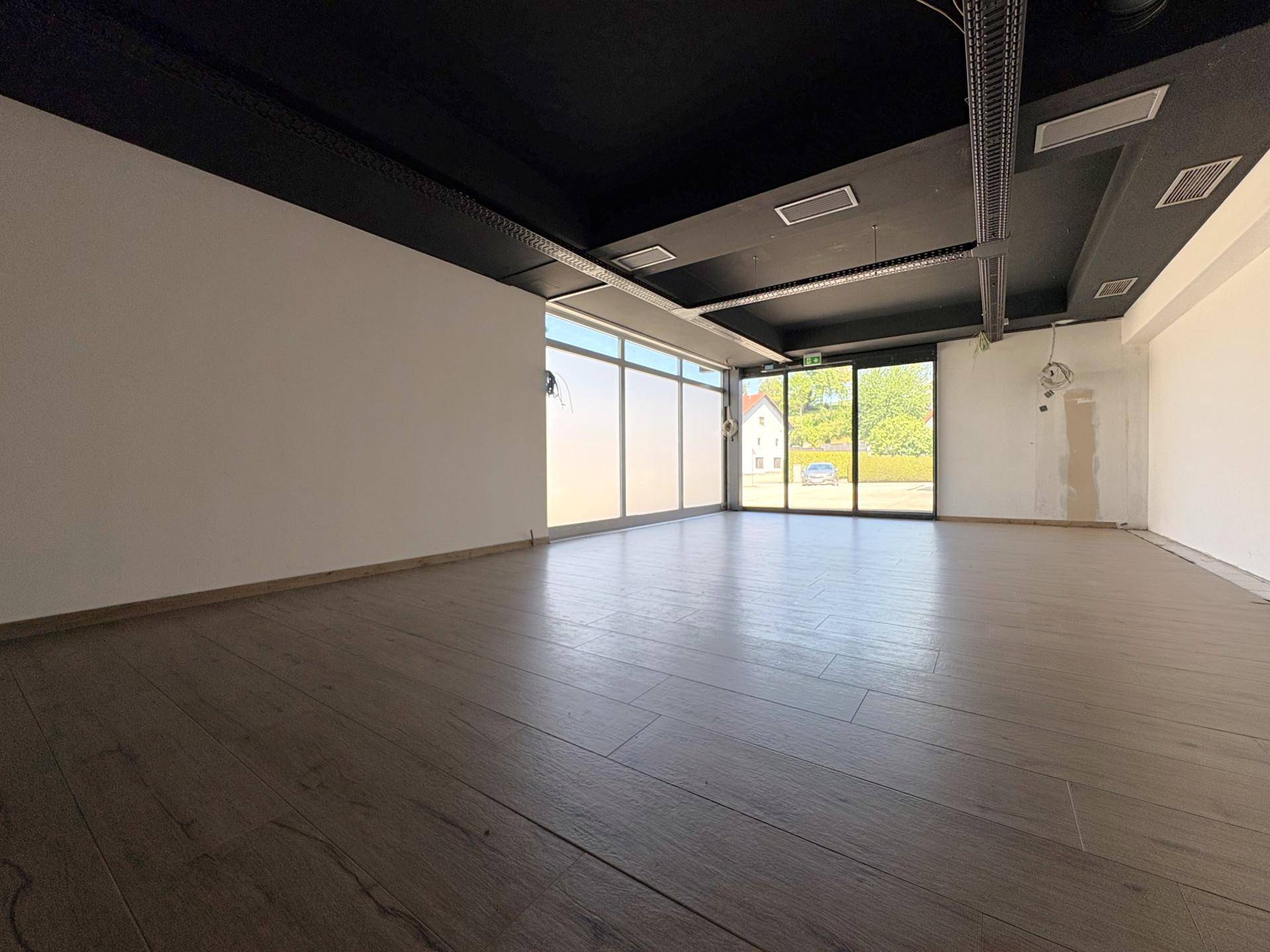 Heller Verkaufsraum mit dunkler Decke, Holzoptik-Boden und großen Schaufenstern zur Straße.