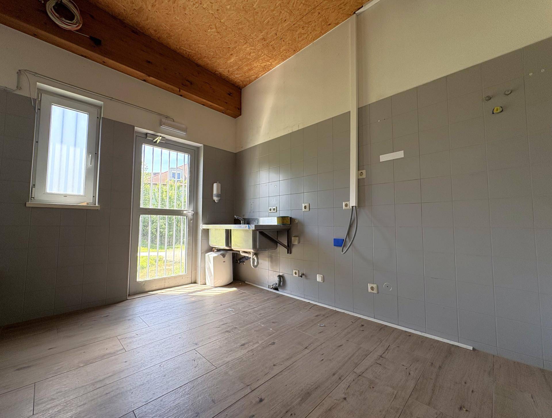 Hauswirtschaftsraum mit Waschbecken, Fliesenwand und Holzoptik-Boden, mit Fenster und Tür zum Garten.