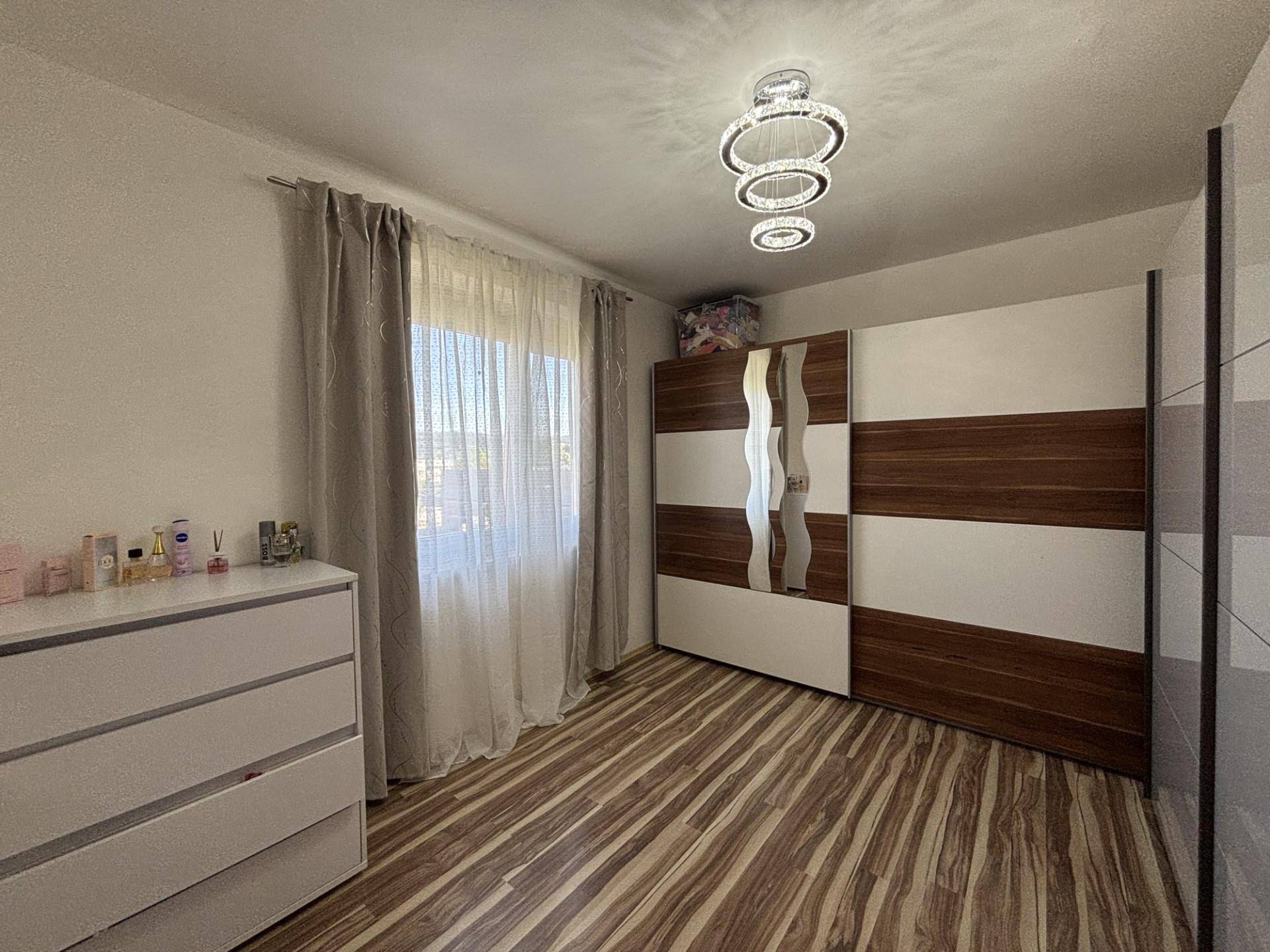 Schlafzimmer mit großem Kleiderschrank, Kommode und Fenster mit viel Tageslicht.