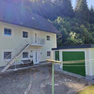 Einfamilienhaus mit hellgrüner Fassade, Satteldach, externer Treppe und grüner Garagentür, umgeben von Natur.