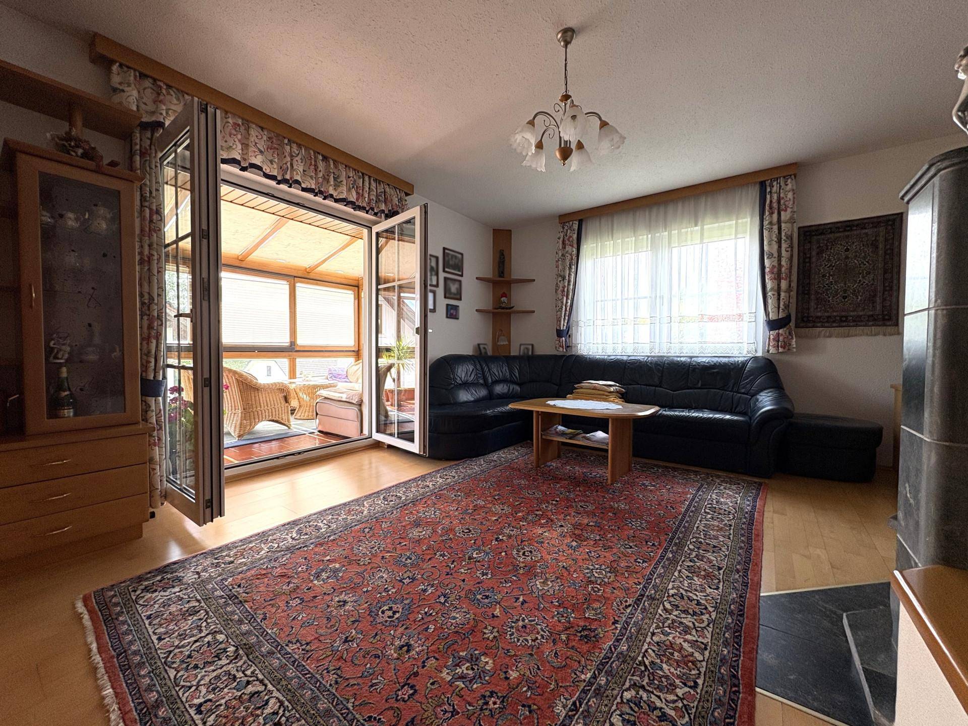 Gemütliches Wohnzimmer mit traditionellem Teppich, Ledersofa und Zugang zum Wintergarten.