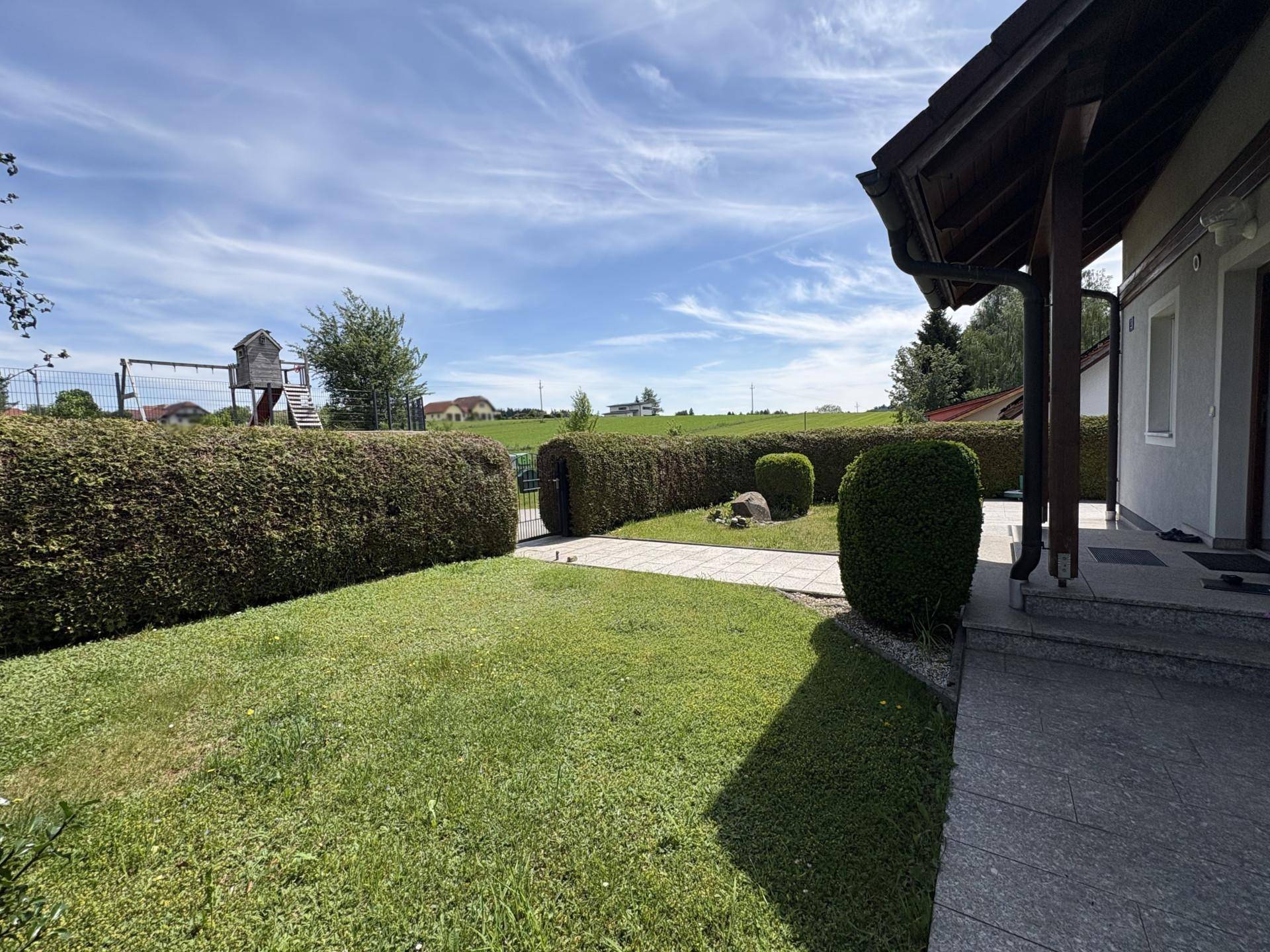 Gepflegter Gartenbereich mit Rasenfläche, Hecke und Kinderspielplatz im Hintergrund.