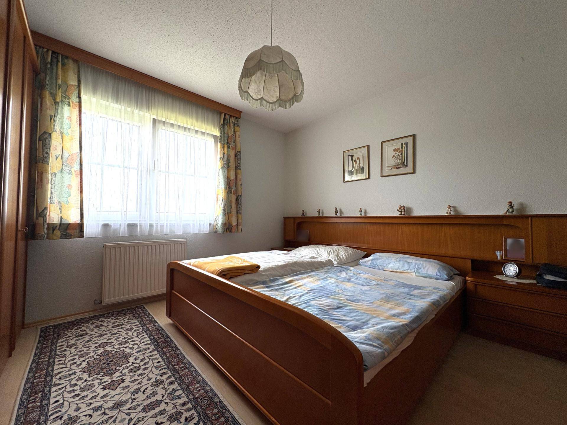 Helles Schlafzimmer mit Doppelbett, Holzmöbeln und Teppichboden.