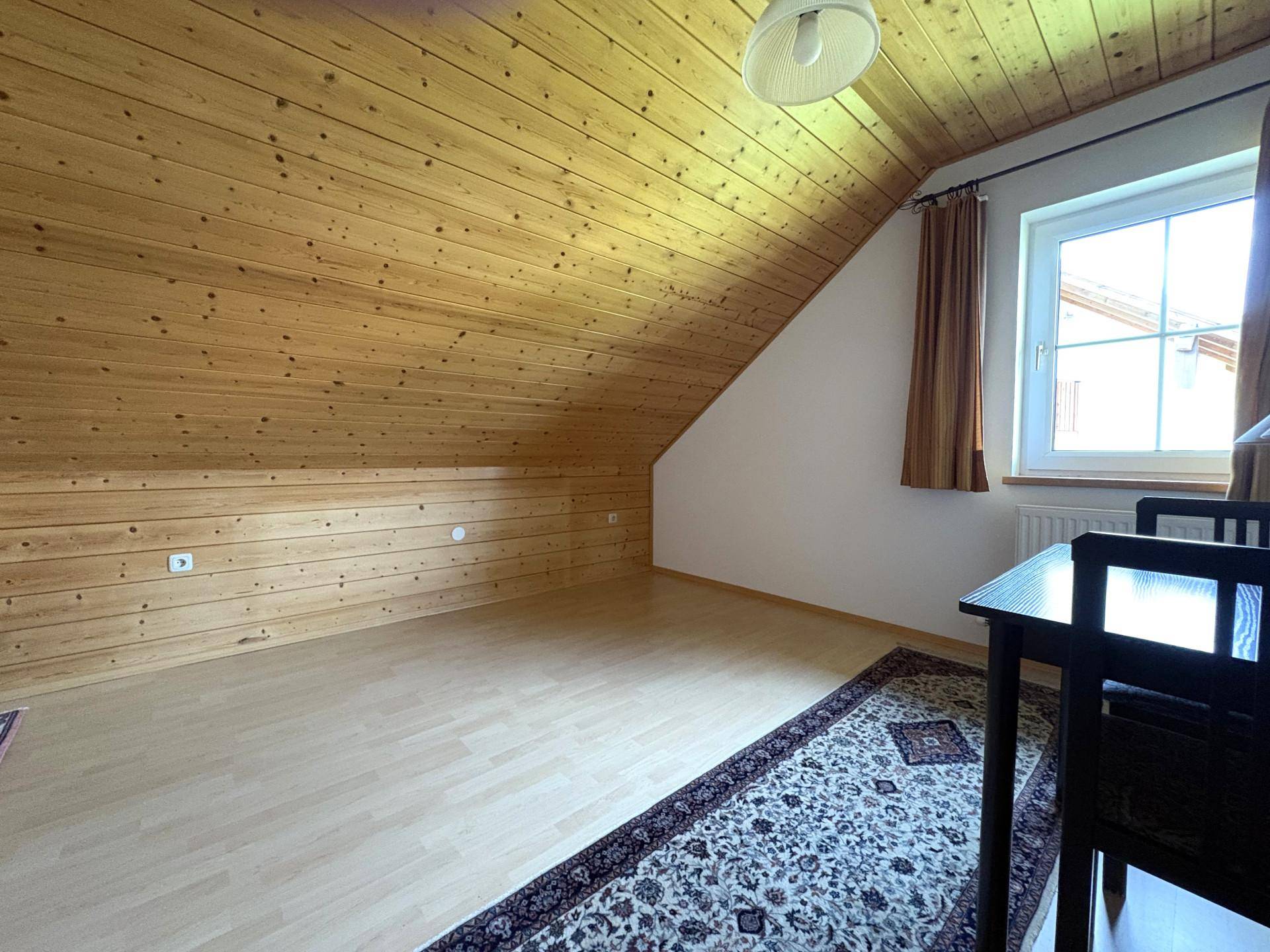 Geräumiges Schlafzimmer im Dachgeschoss mit Holzverkleidung und Laminatboden.