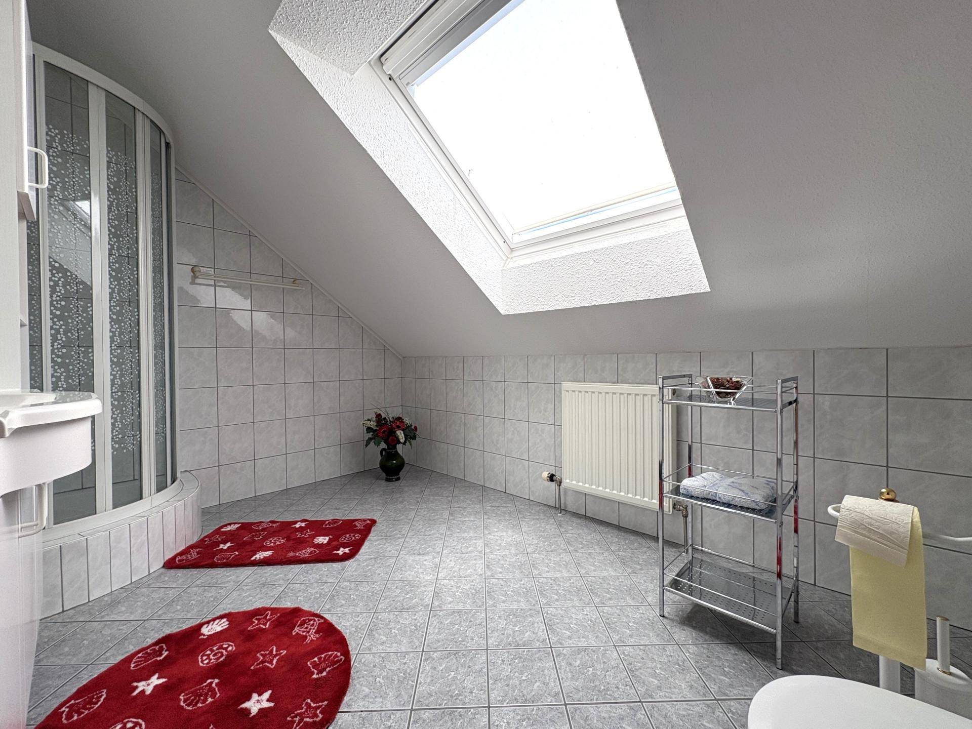 Helles Badezimmer im Dachgeschoss mit Dusche, Dachfenster und hellgrauen Fliesen.