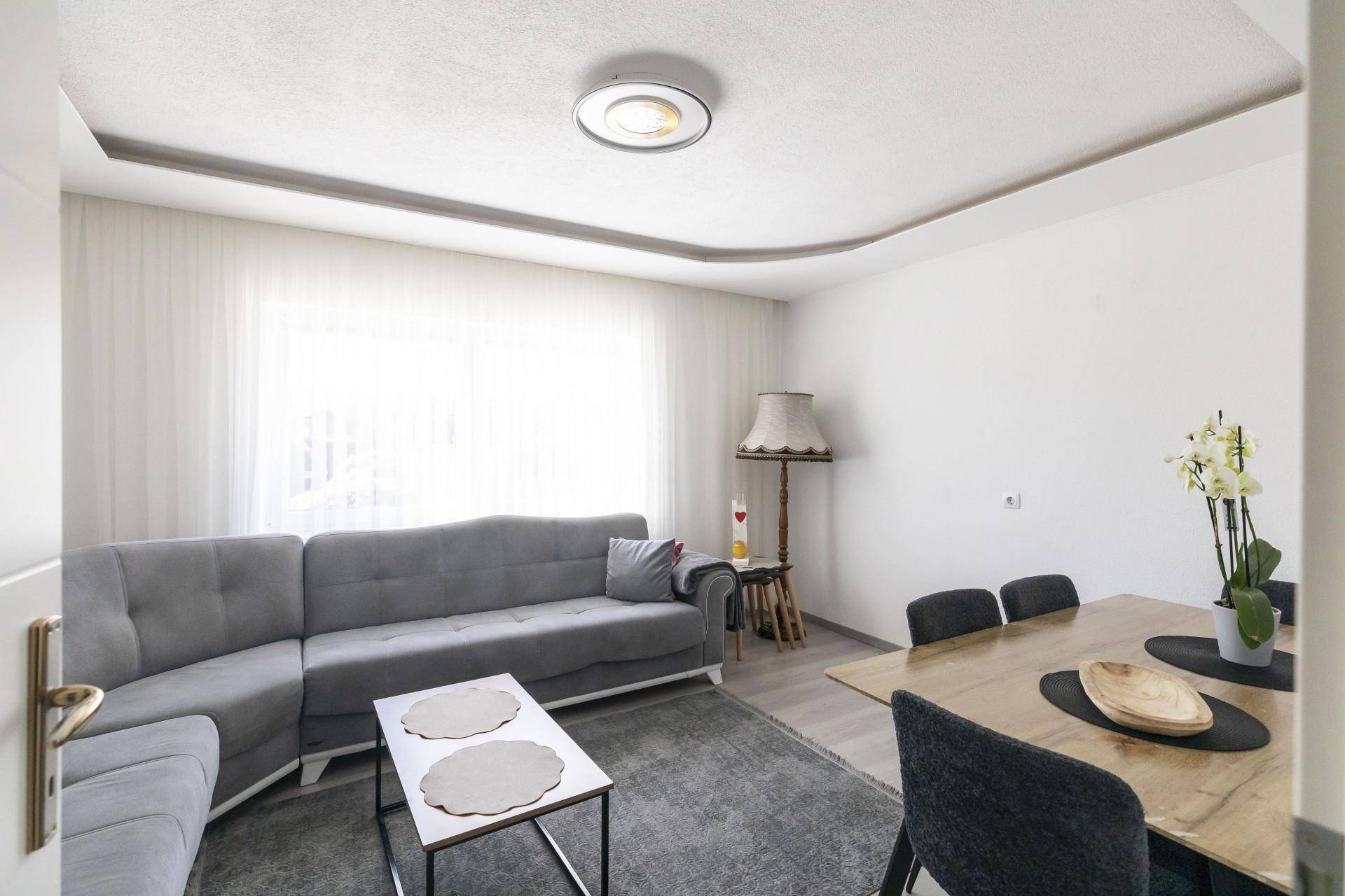 Kombinierter Wohn- und Essbereich mit grauem Ecksofa und hellem Holztisch.