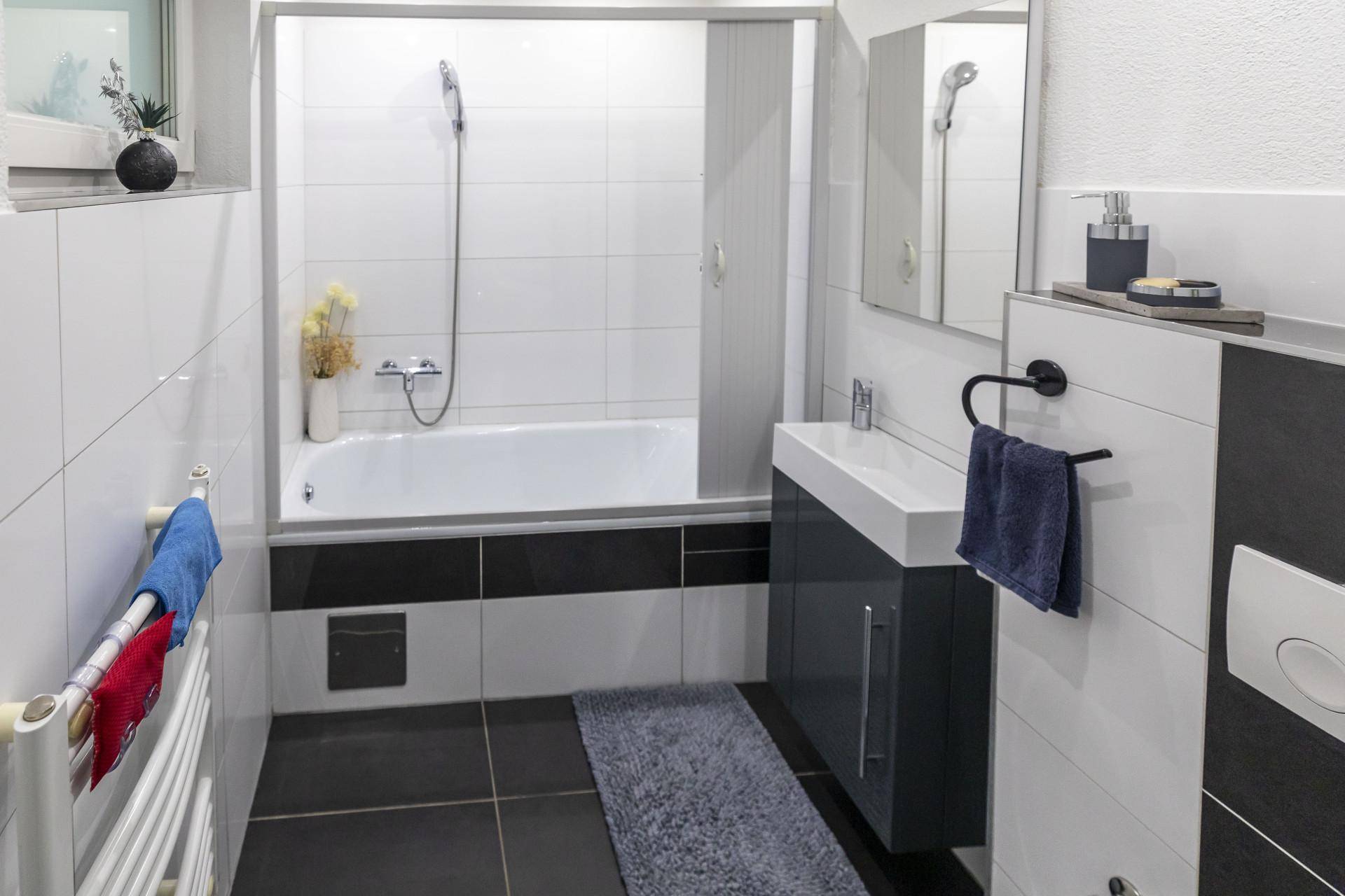 Modernes Badezimmer mit Badewanne, Duschfunktion und kontrastreichen Schwarz-Weiß-Fliesen.