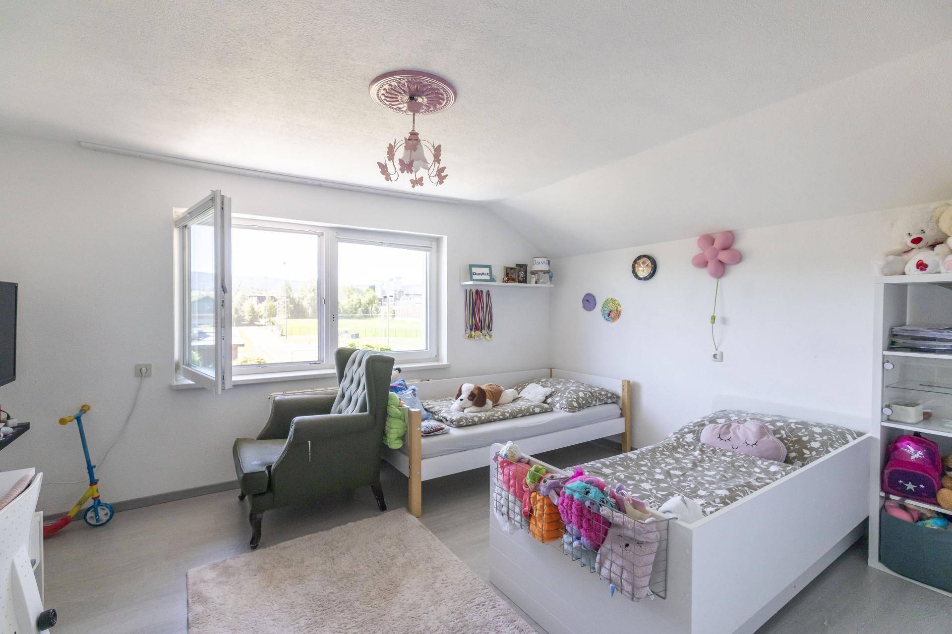 Kinderzimmer mit zwei Betten, großem Fenster und Blick ins Grüne.