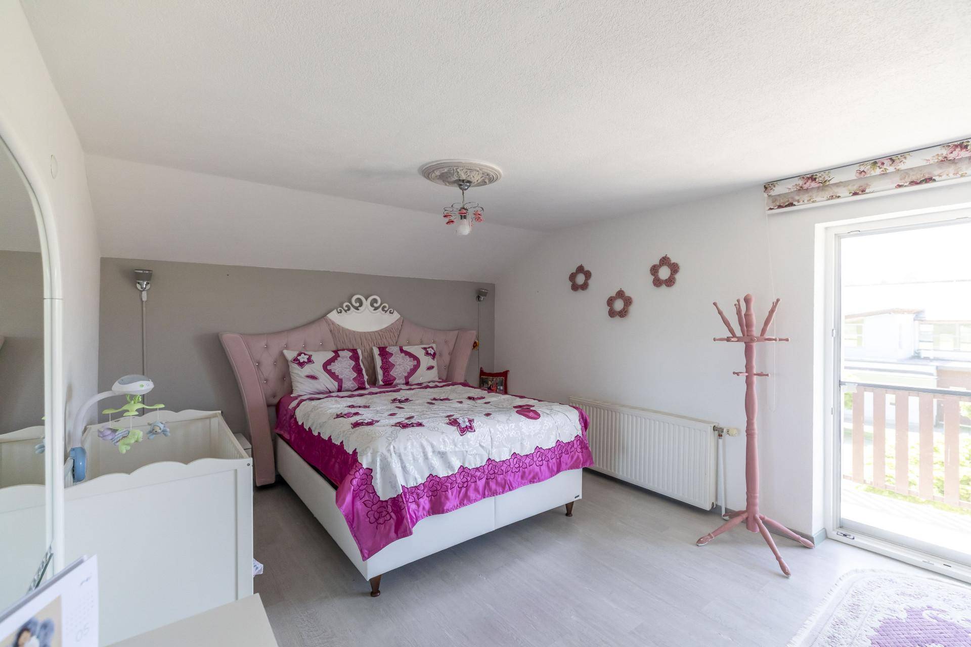 Schlafzimmer mit Doppelbett, rosa Akzenten und Zugang zum Balkon.