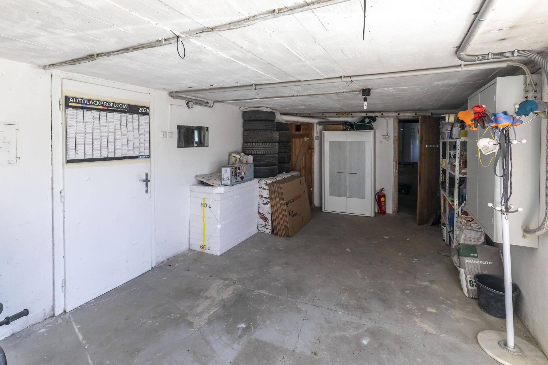Geräumige Garage mit Betonboden und Abstellmöglichkeiten für Reifen und Geräte.