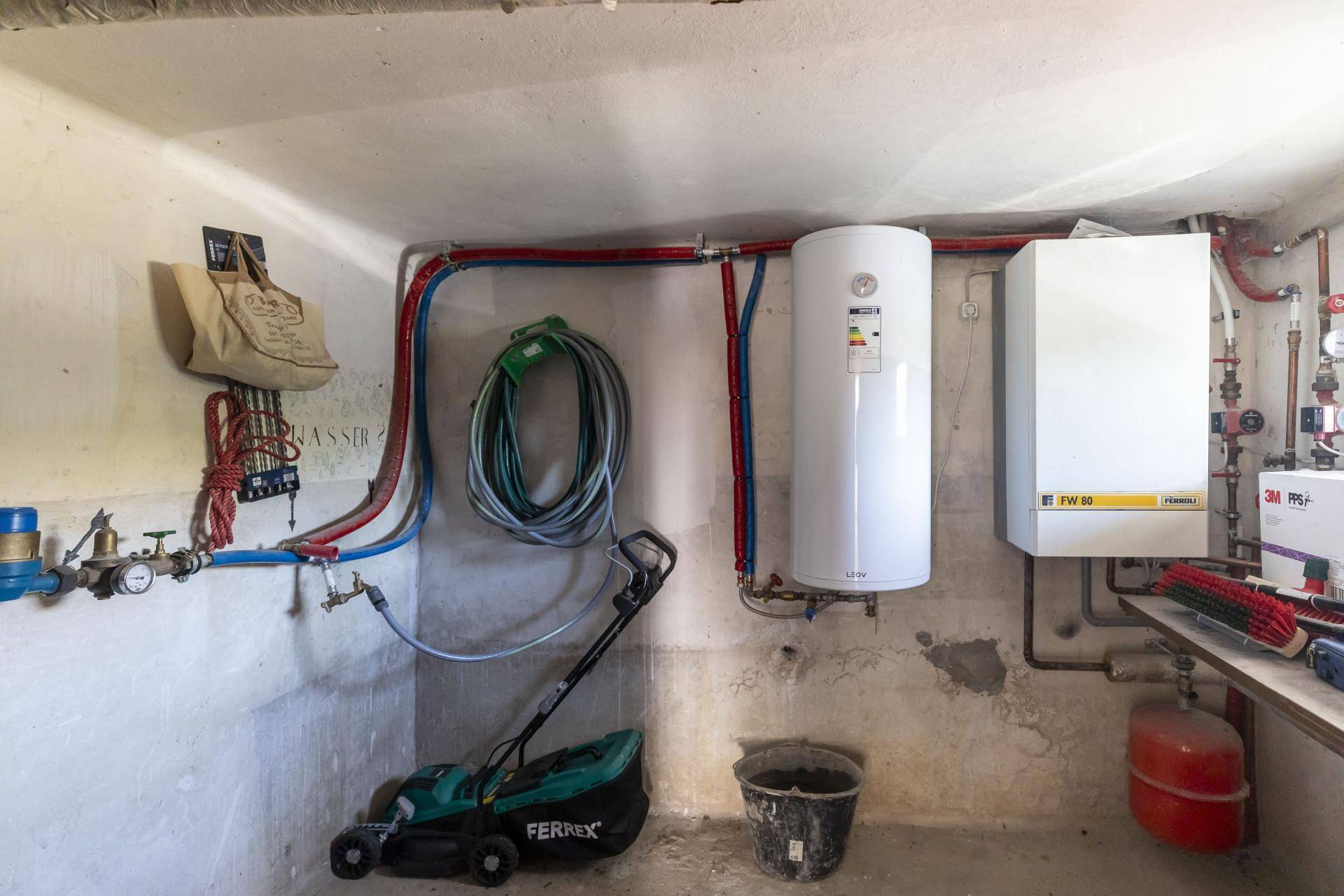 Technikraum mit Warmwasserbereiter, Heizungsanlage und Gartengeräten.