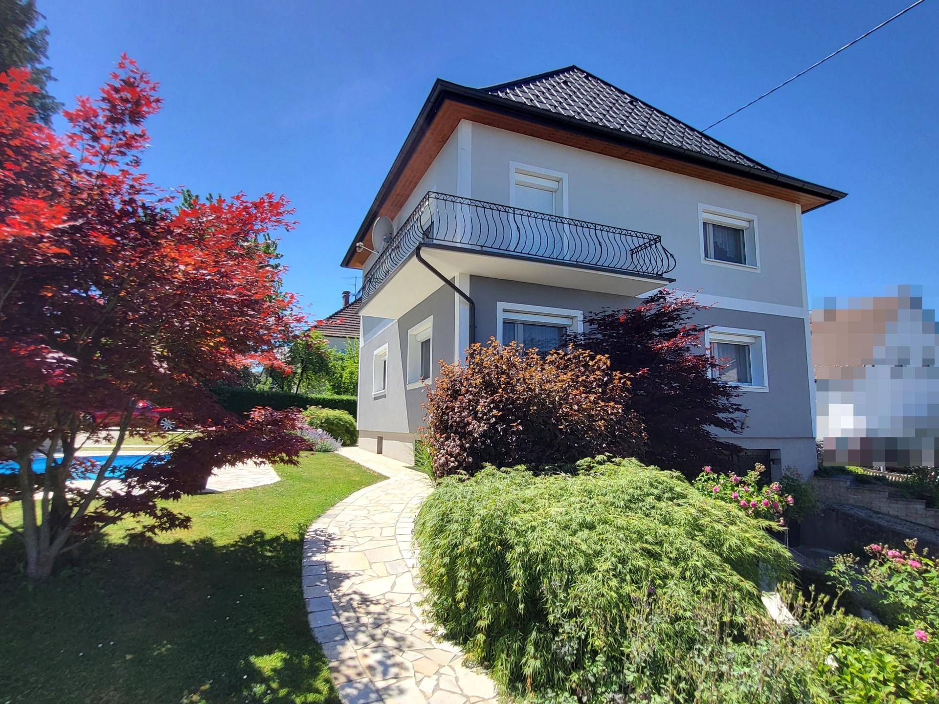 Hausansicht mit Garten, Pool und rotem Ahornbaum unter blauem Himmel.