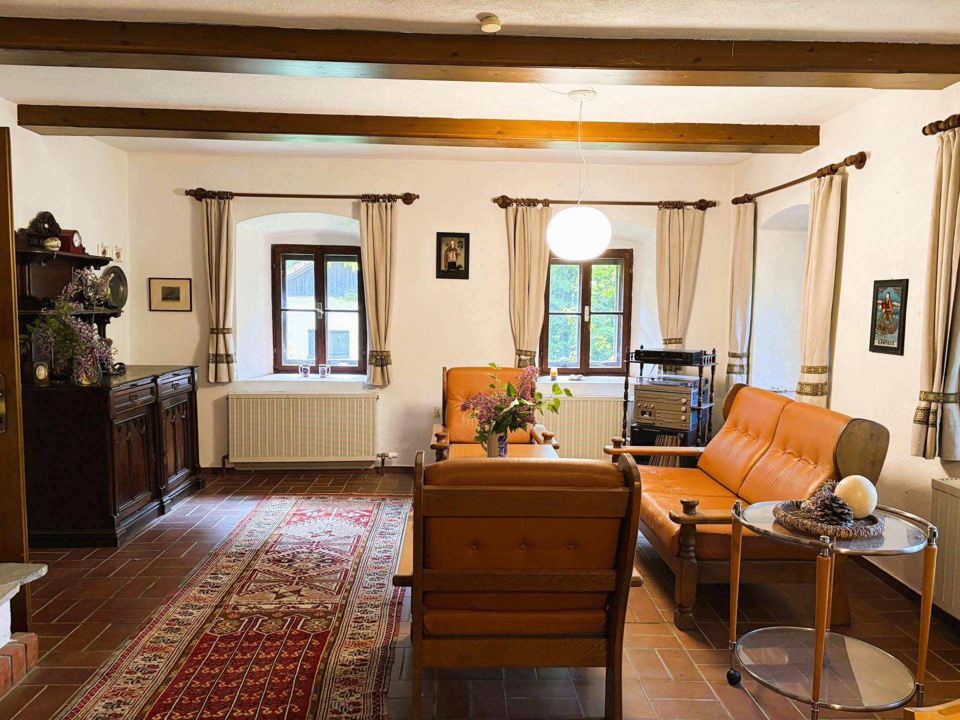 Geräumiges Wohnzimmer mit Terrakotta-Fliesen, Holzbalken und einem großen Orientteppich, gemütlich eingerichtet.