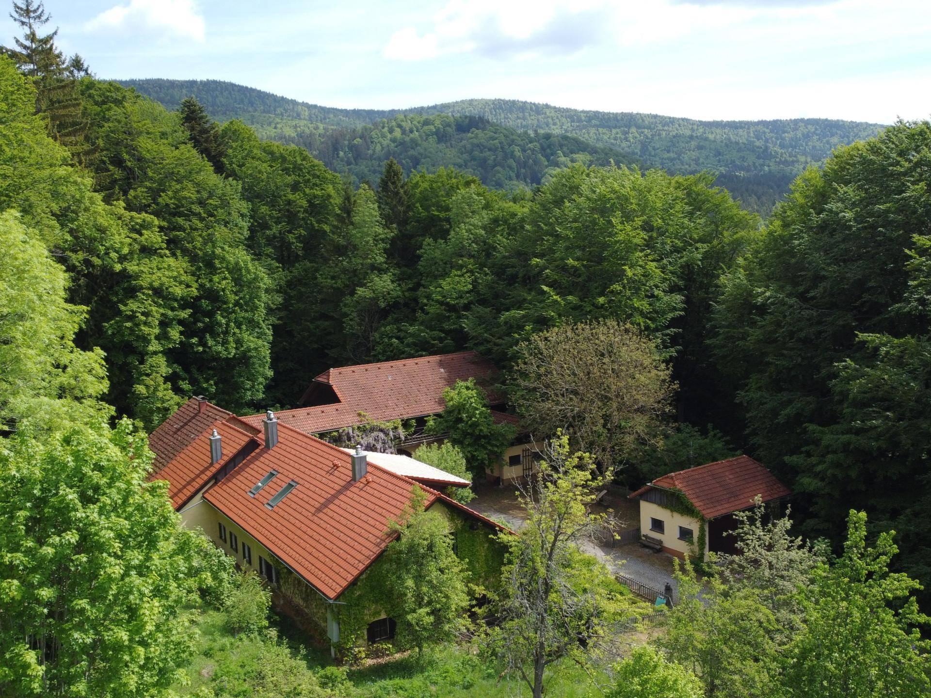 Panoramablick auf das Anwesen, eingebettet in ein Tal mit bewaldeten Hügeln und grüner Landschaft.