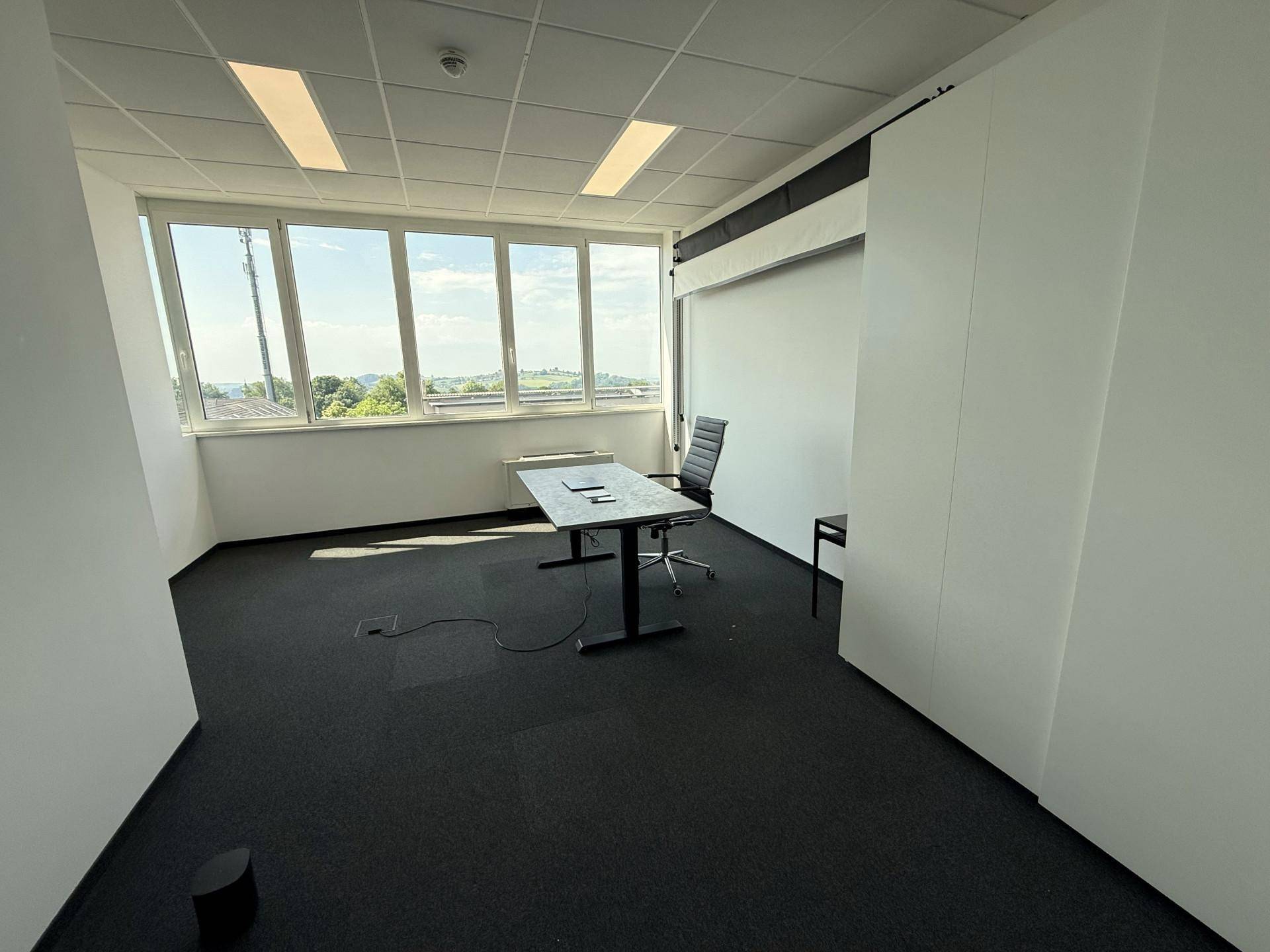 Leeres, helles Büro mit einem Schreibtisch, Bürostuhl und weitem Ausblick durch die Fensterfront.
