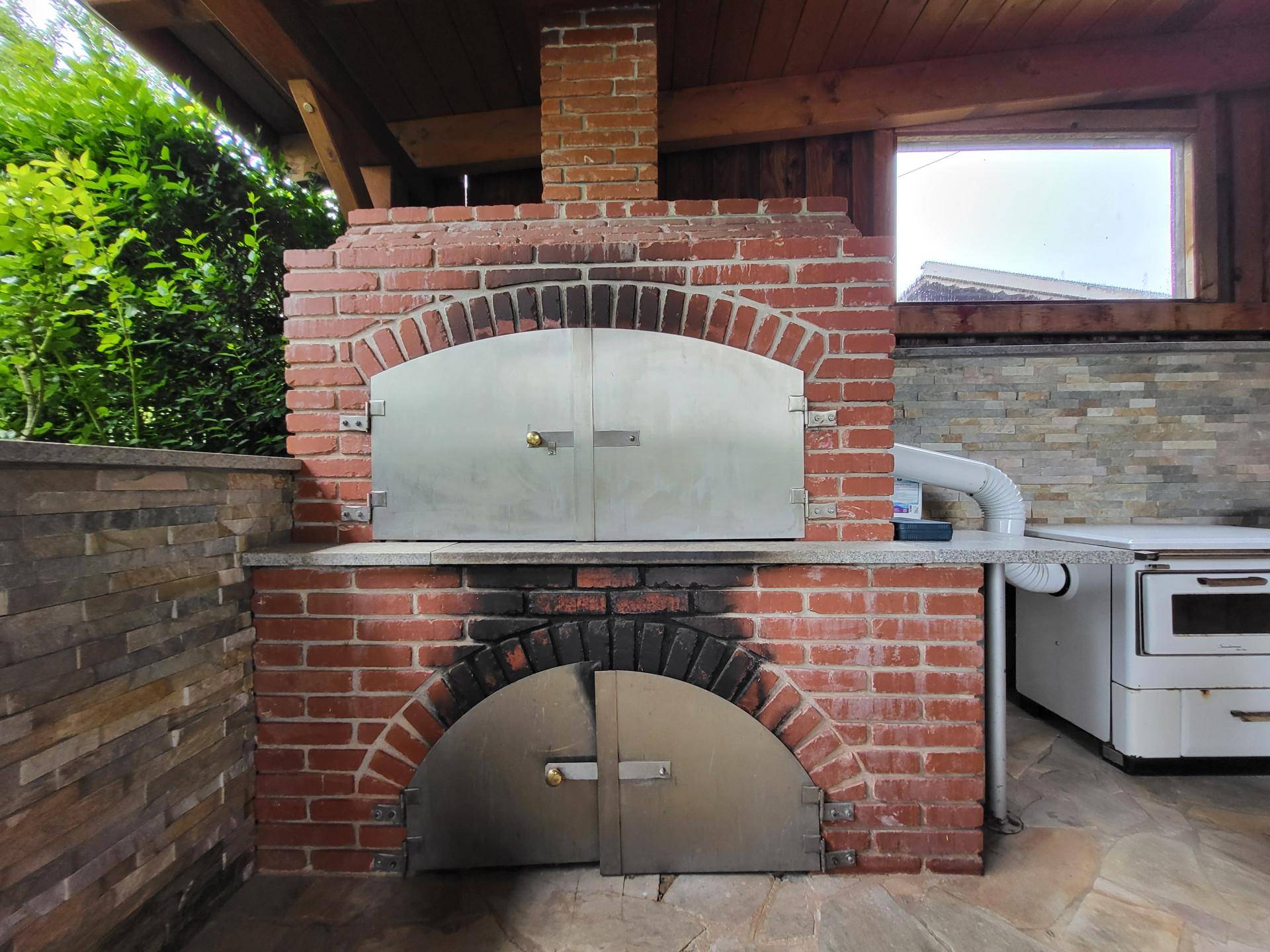 Gemauerter Außenofen mit Metalltüren, ideal für Pizza und Brotbacken.