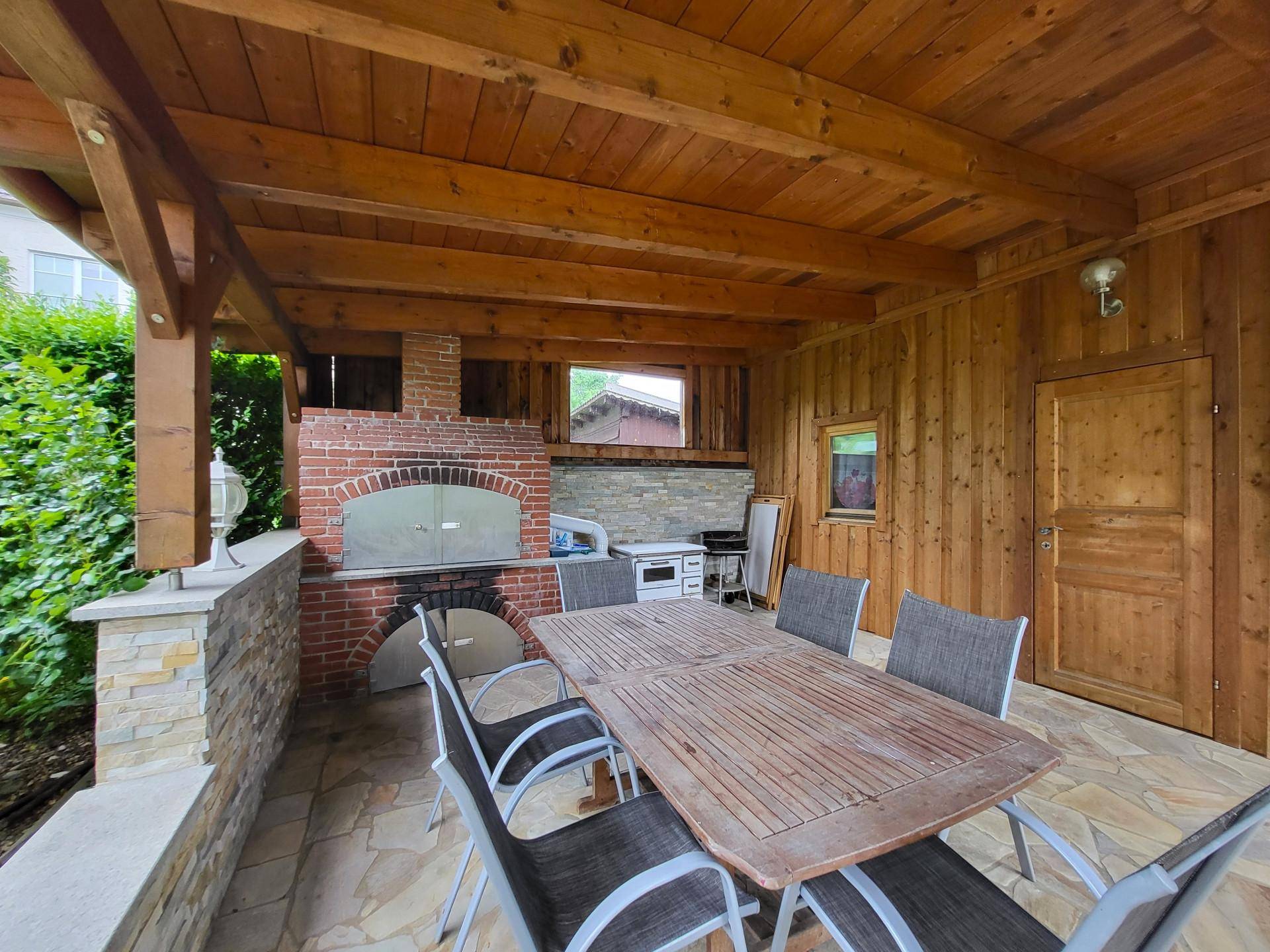 Überdachte Terrasse mit Holzdach, Esstisch und gemauertem Pizzaofen.