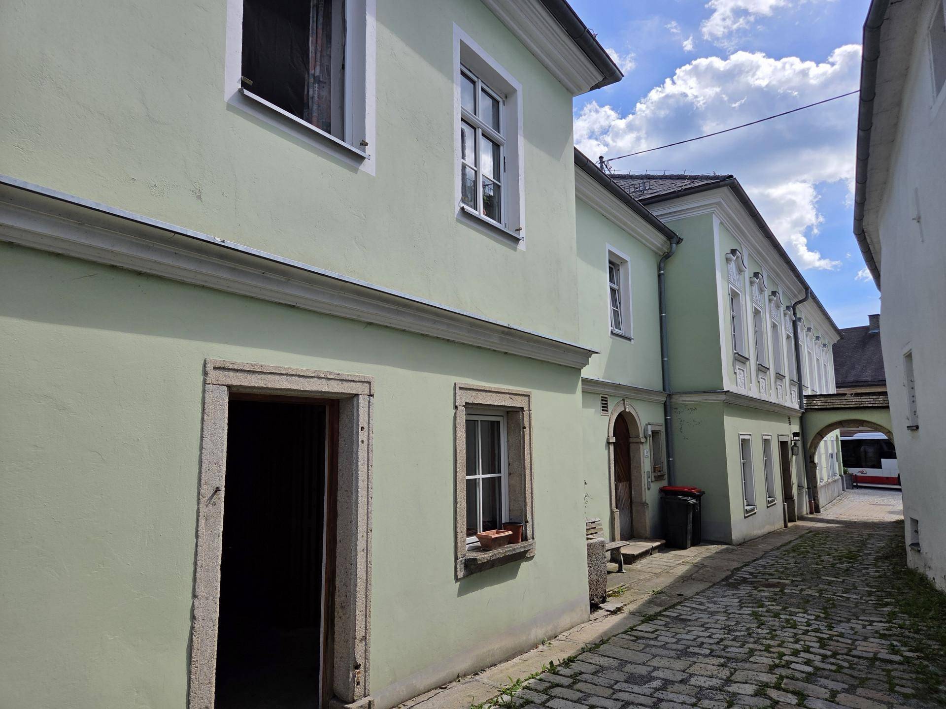 Historisches Gebäude mit hellgrüner Fassade und gepflasterter Gasse unter blauem Himmel.