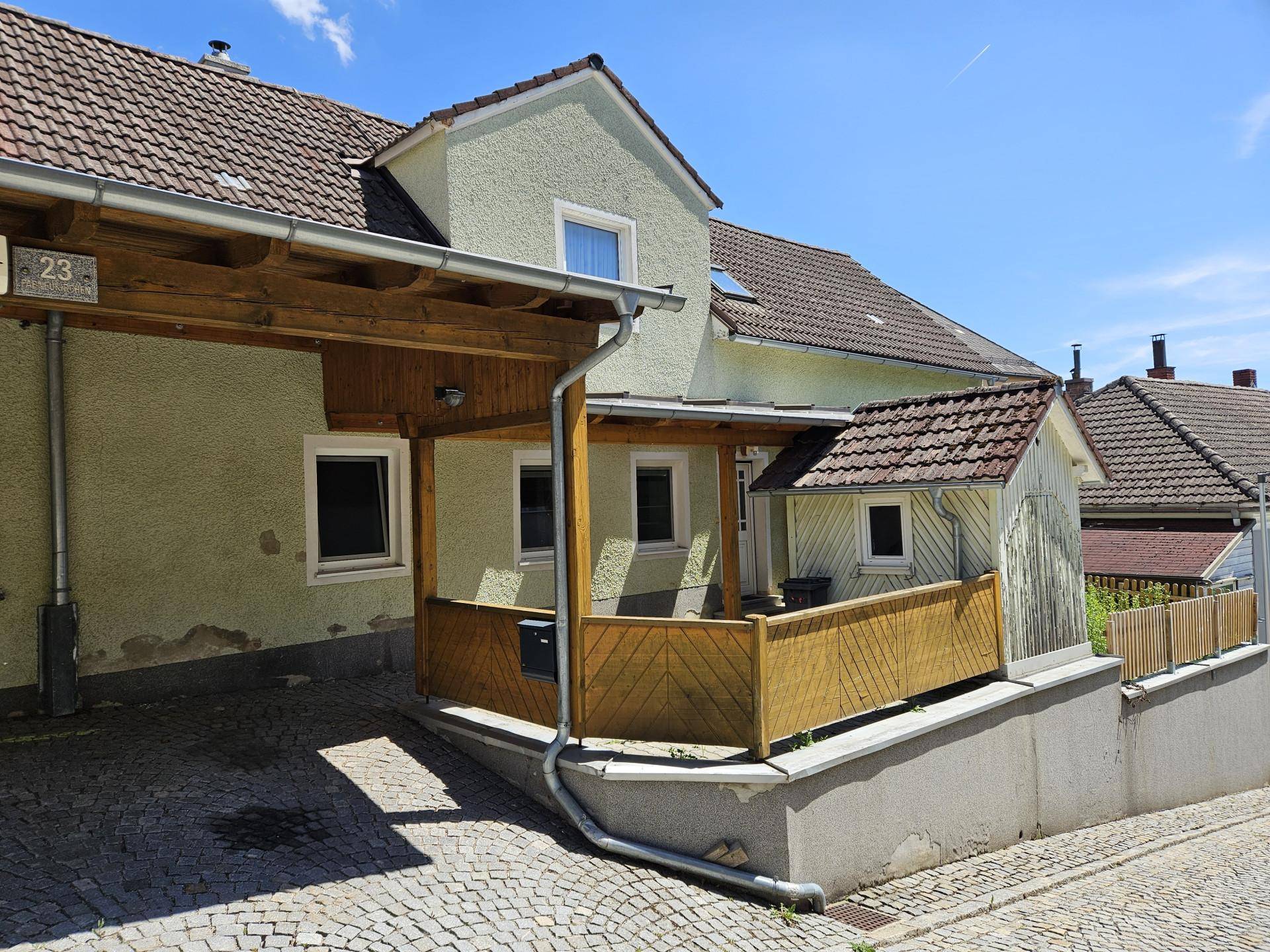 Seitenansicht des Wohnhauses mit überdachtem Carport und gepflasterter Zufahrt bei Sonnenschein.